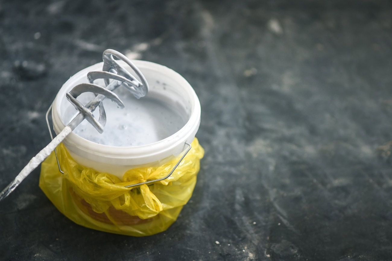 Taza pequeña blanca con un batidor de metal encima, envuelta en una bolsa de plástico amarilla sobre una superficie oscura.