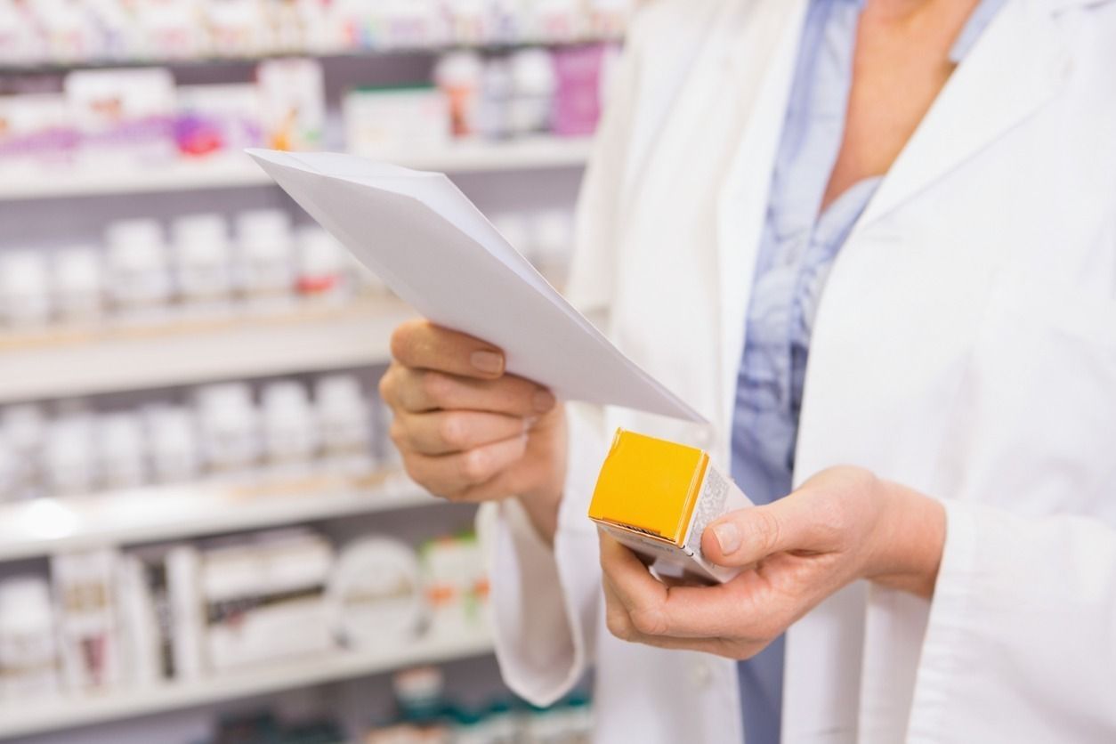 Una farmacéutica sostiene un frasco de pastillas y una receta en una farmacia.
