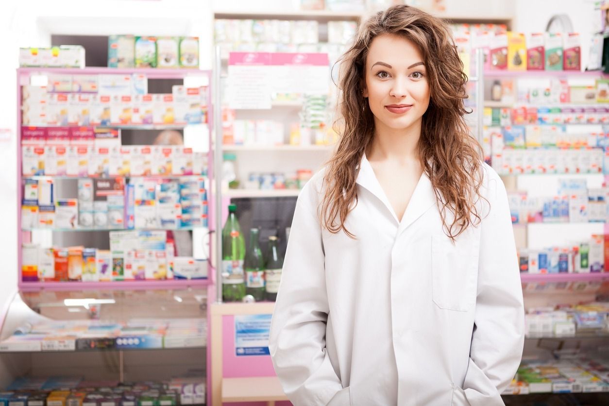 Una farmacéutica está de pie en una farmacia con las manos en los bolsillos.