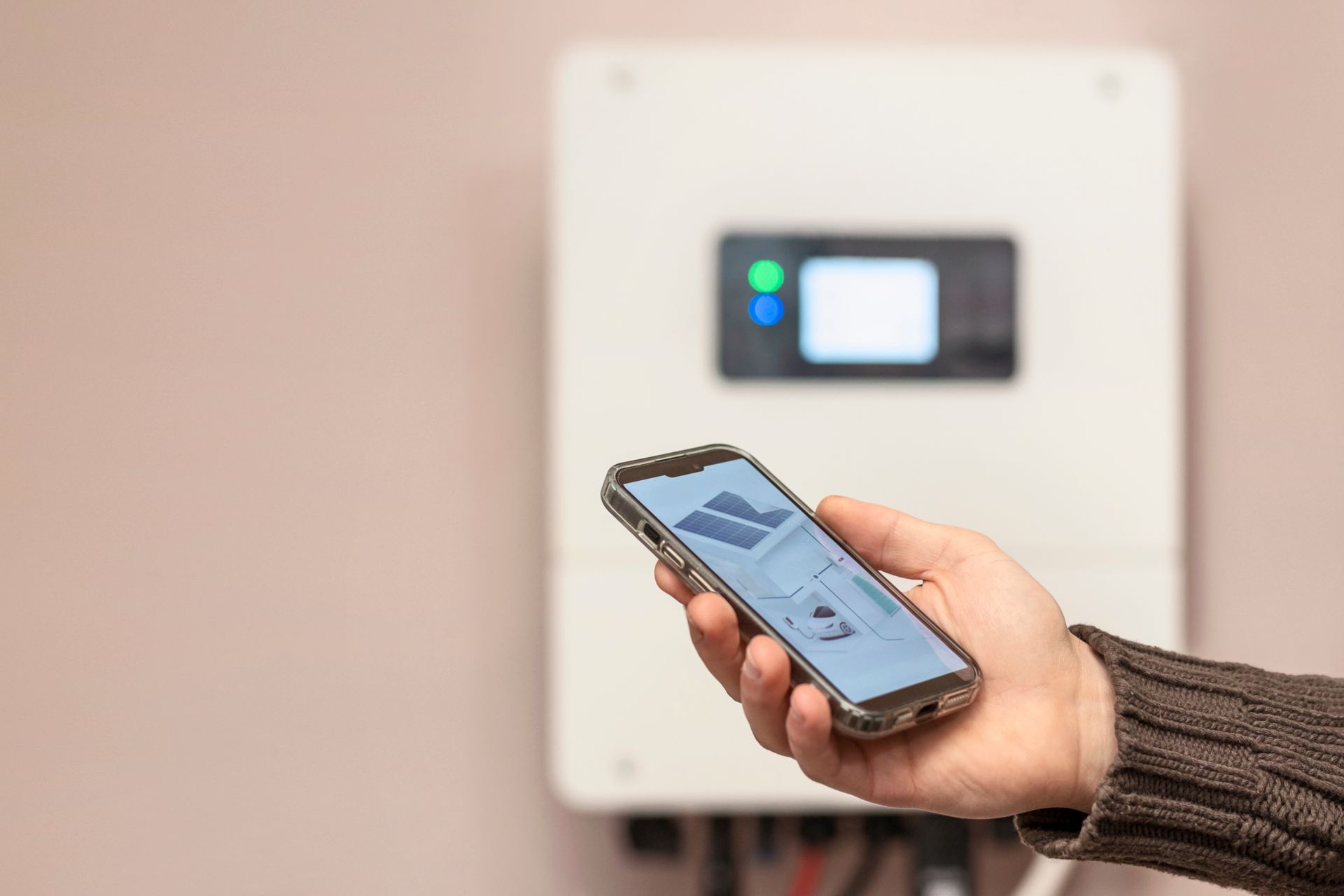 Une main tient un smartphone affichant une application de surveillance de l'énergie solaire devant un onduleur solaire.