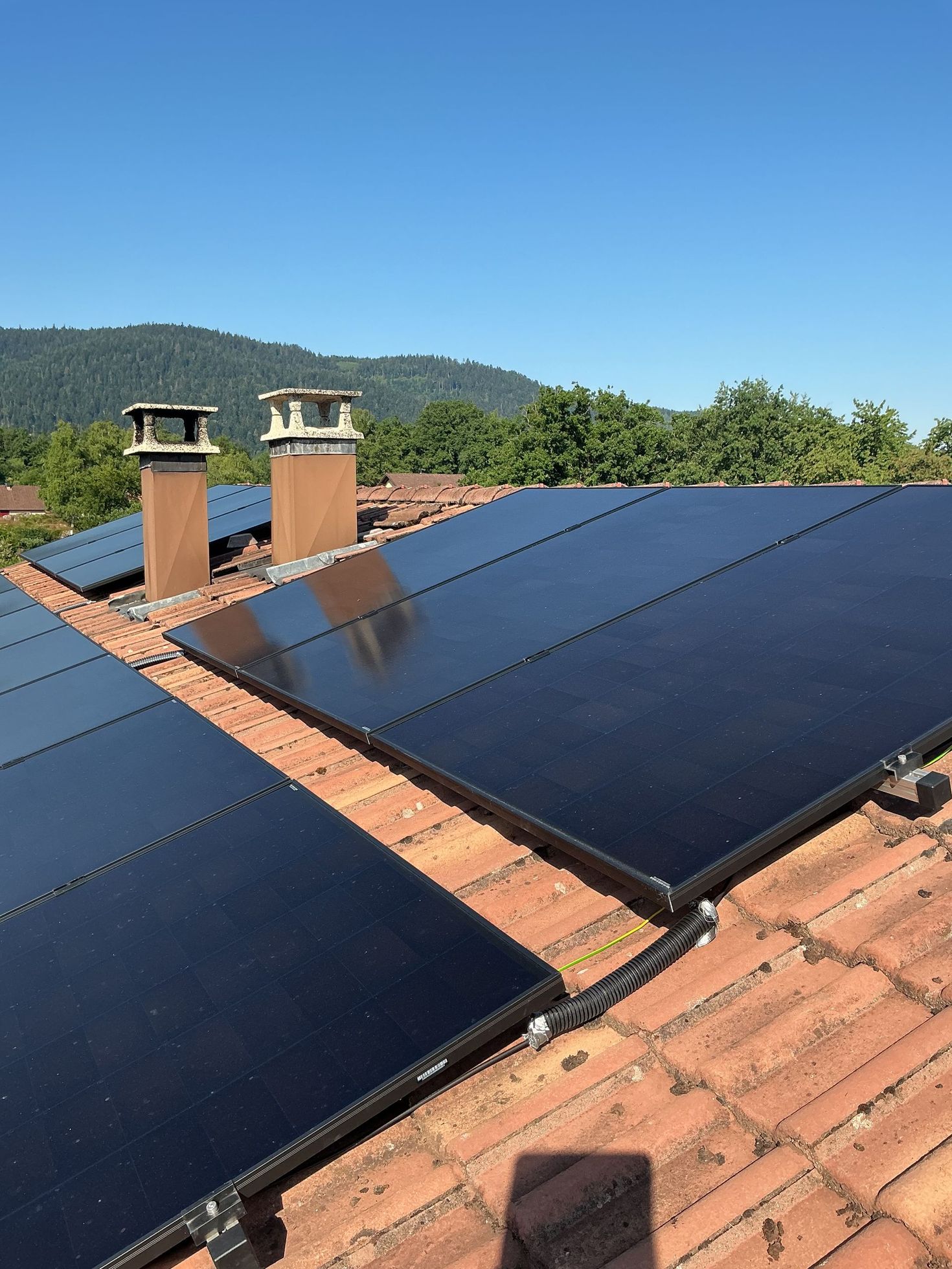 Des panneaux solaires installés sur un toit de tuiles en terre cuite, avec deux cheminées en briques.