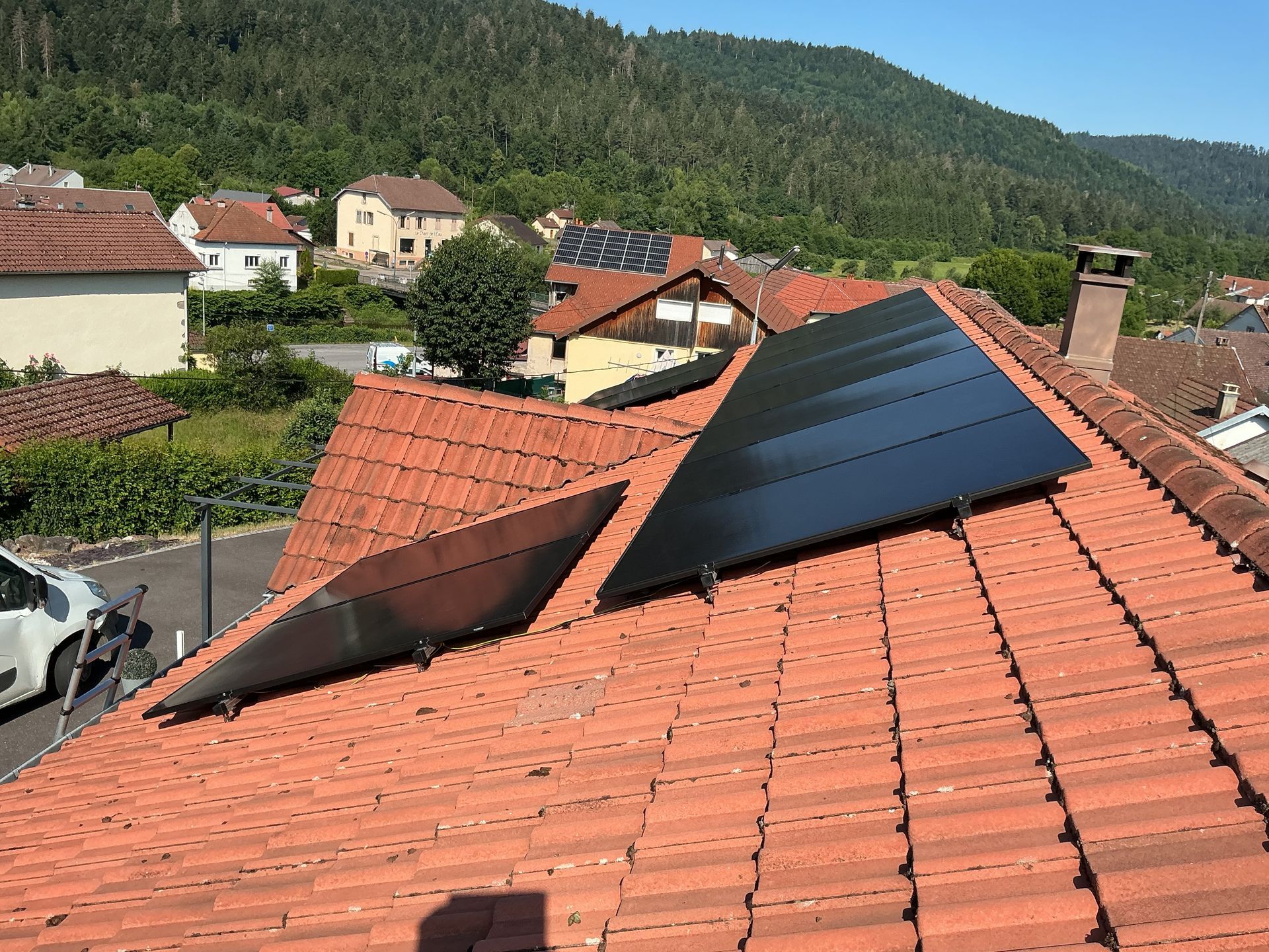 Des panneaux solaires noirs sont installés sur un toit de tuiles rouges en pente, donnant sur un quartier résidentiel arboré.