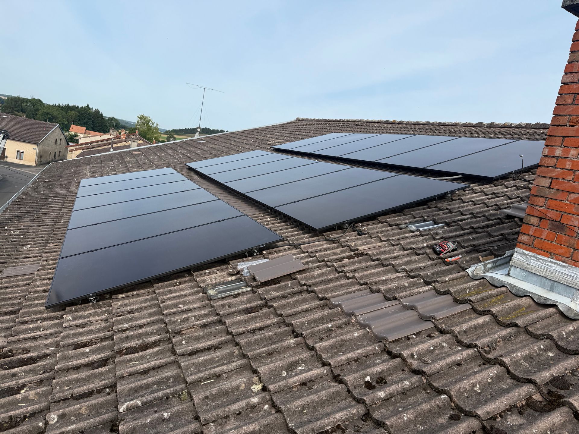 Une maison au toit recouvert de panneaux solaires, avec des murs extérieurs blancs et gris foncé sous un ciel nuageux.
