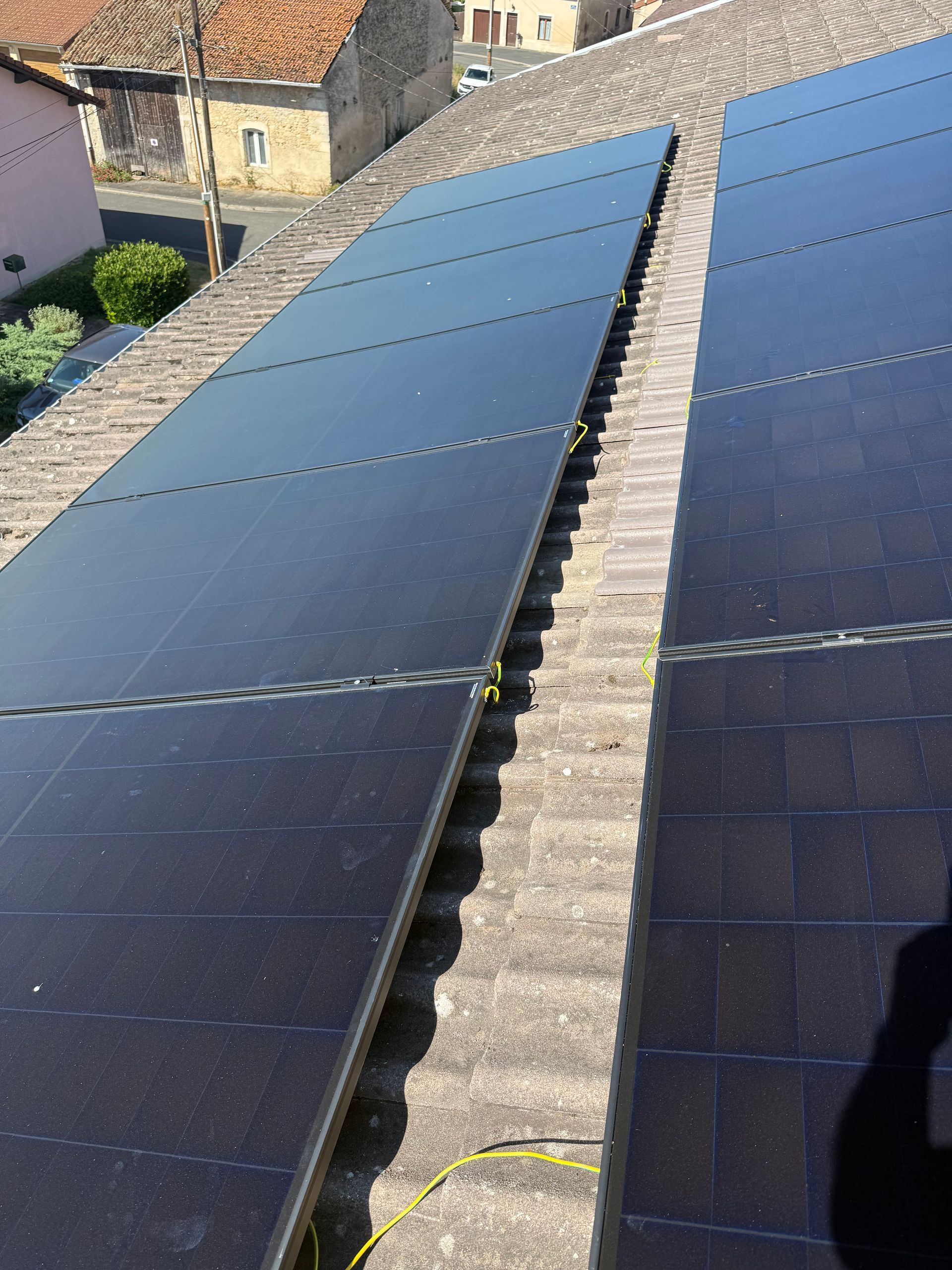 Une personne se tient sur un toit de tuiles à côté de panneaux solaires en cours d'installation.