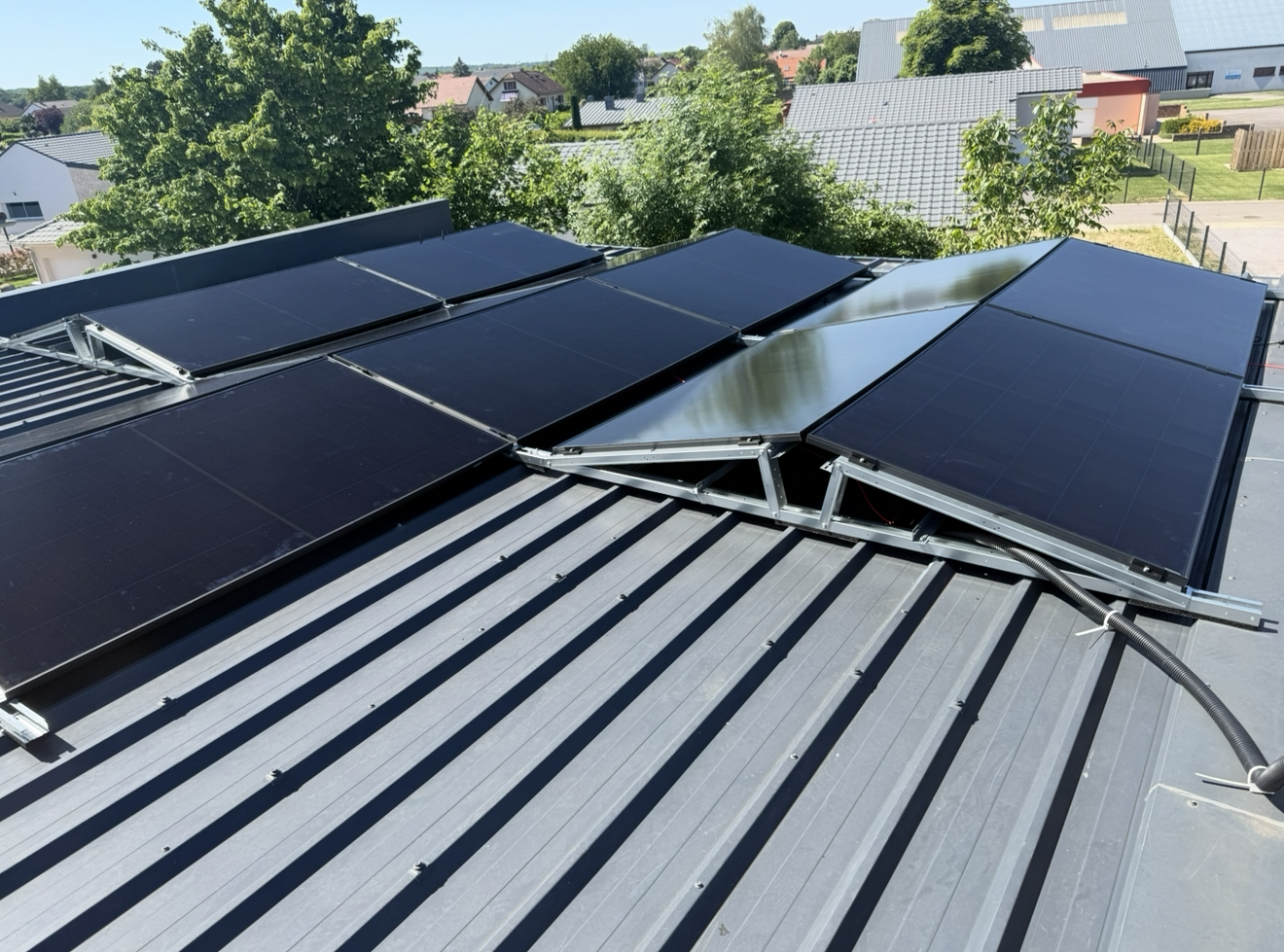 Plusieurs panneaux solaires noirs sont montés sur un toit en tôle ondulée grise, inclinés pour capter la lumière du soleil.