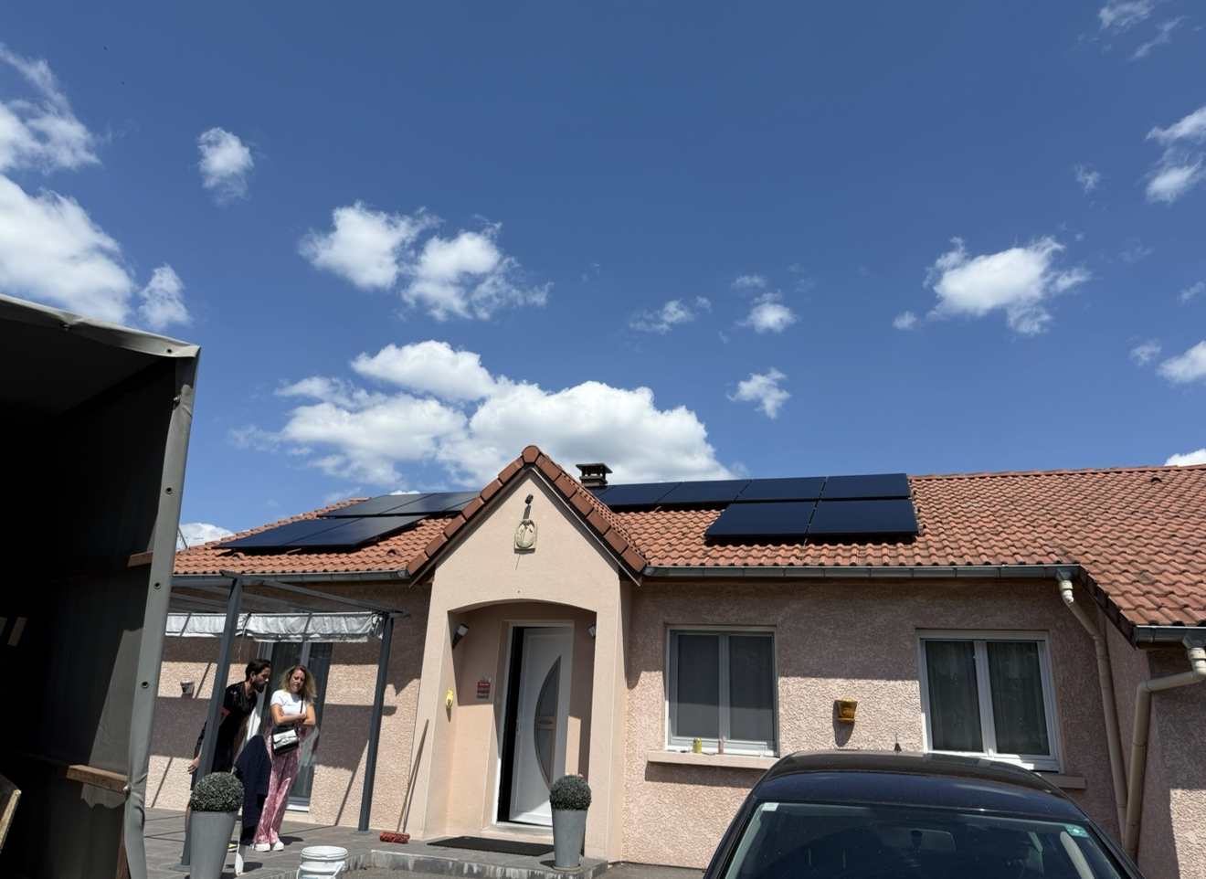Une maison avec des panneaux solaires sur un toit de tuiles sous un ciel bleu ensoleillé.