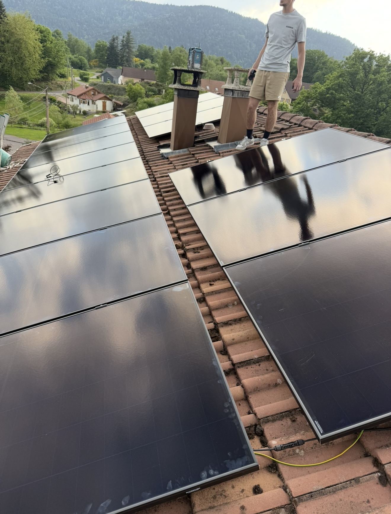 Une personne se tient sur un toit de tuiles à côté de panneaux solaires en cours d'installation.