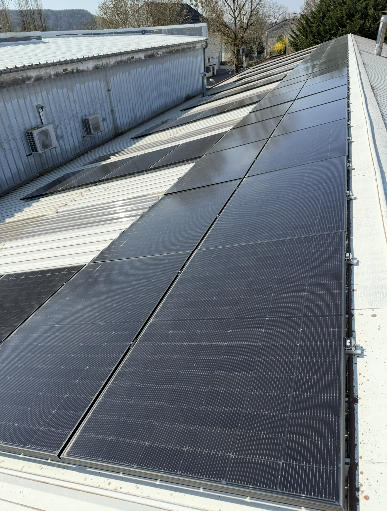 Vue en biais d'un toit métallique avec plusieurs rangées de panneaux solaires noirs installées sur le pourtour.