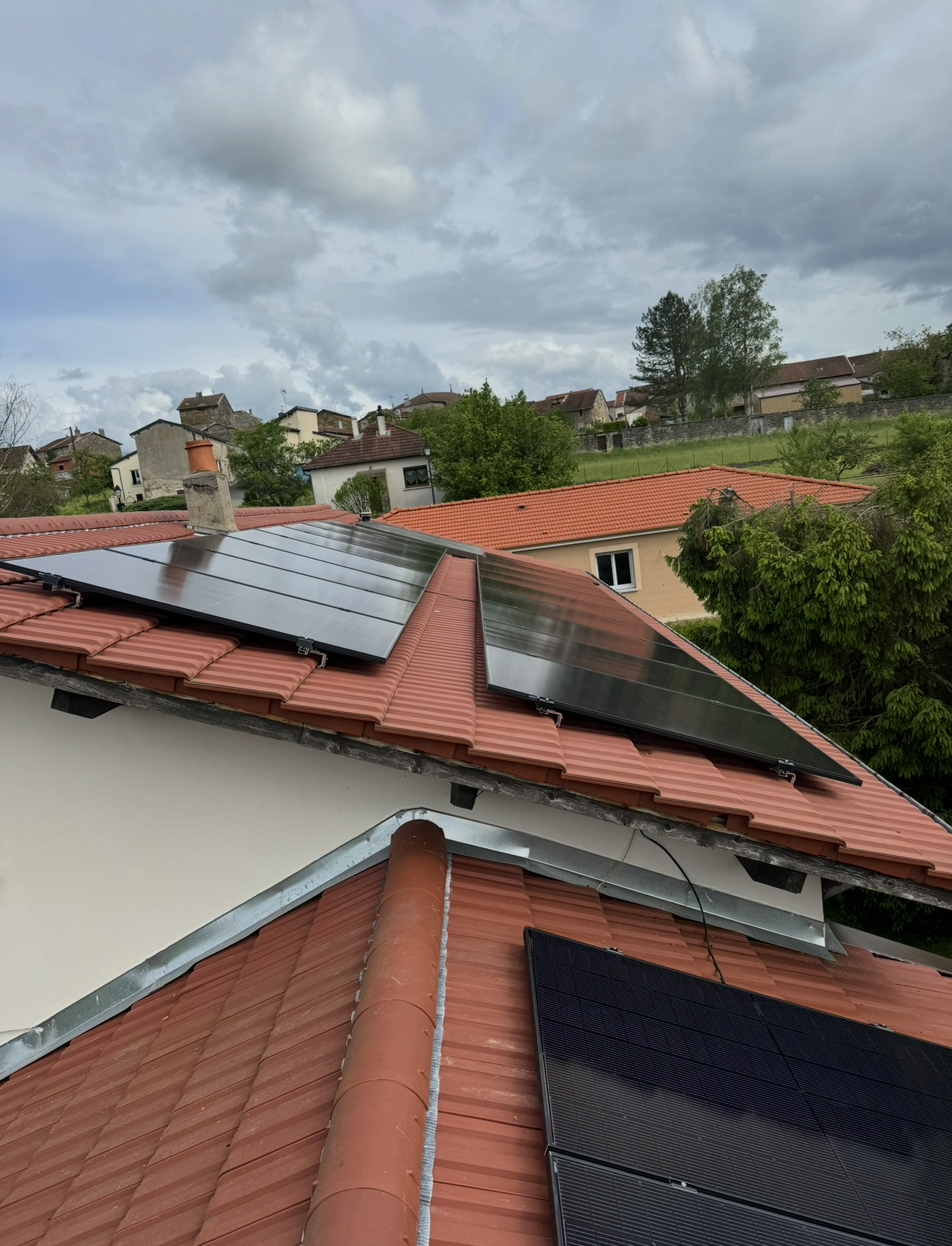 Plusieurs panneaux solaires sont installés sur le toit de tuiles rouges d'une maison d'habitation sous un ciel nuageux.
