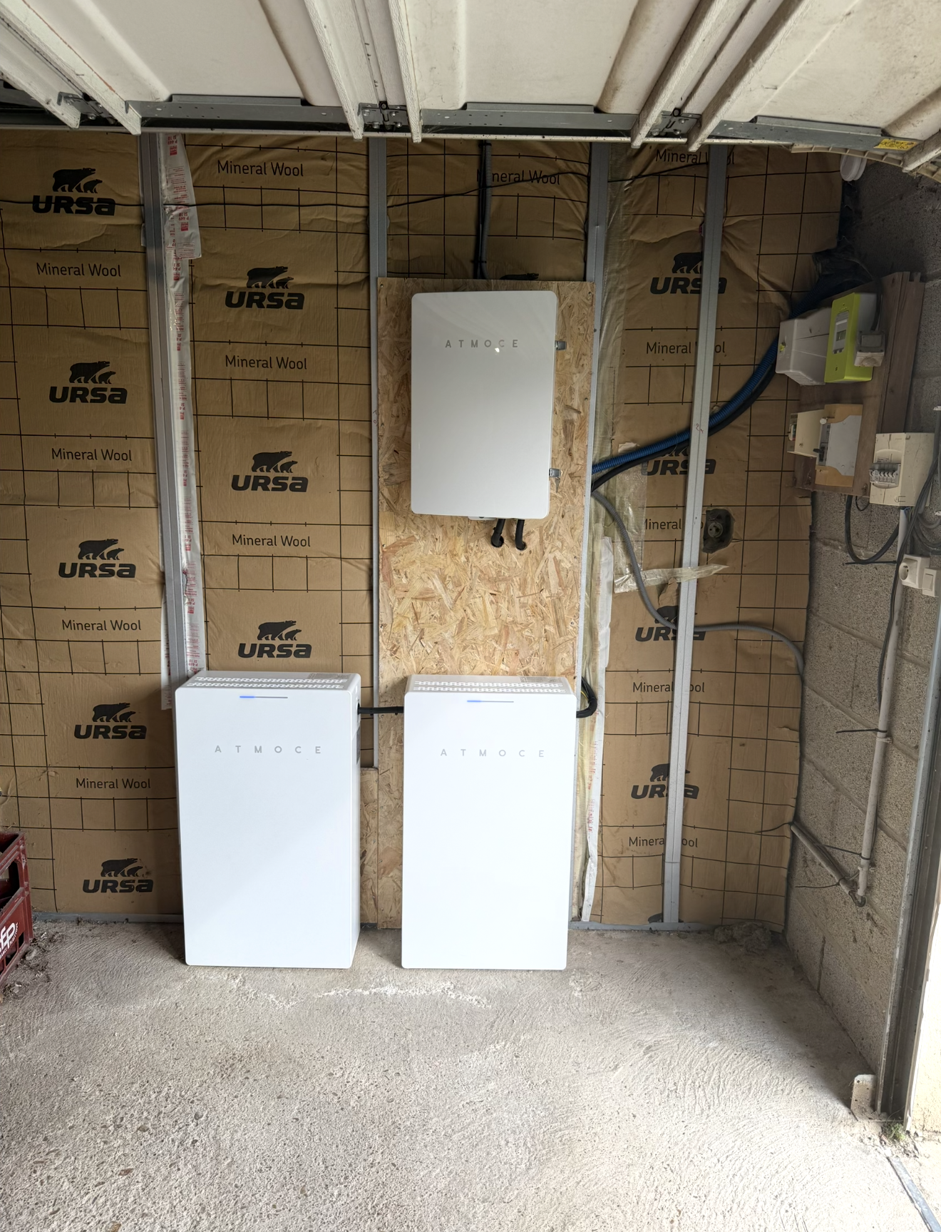 Un onduleur fixé au mur et deux batteries au sol dans un garage.