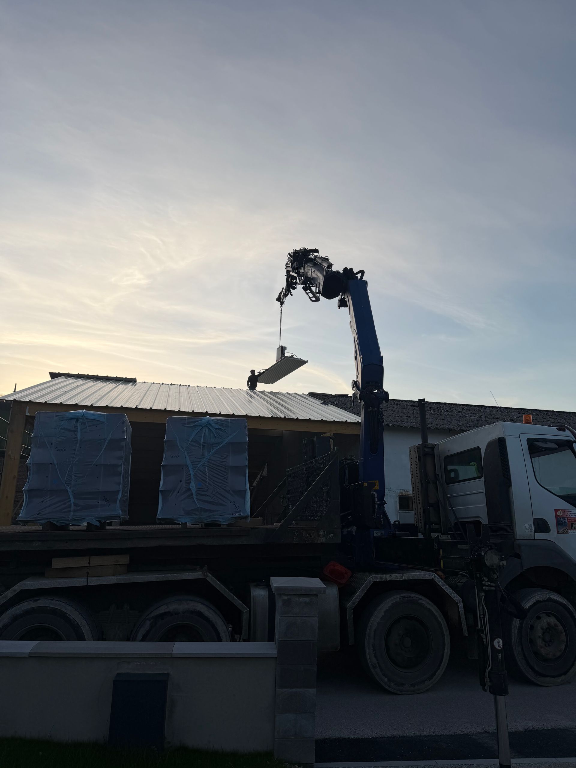 Plusieurs panneaux solaires sont installés sur le toit de tuiles rouges d'une maison d'habitation sous un ciel nuageux.