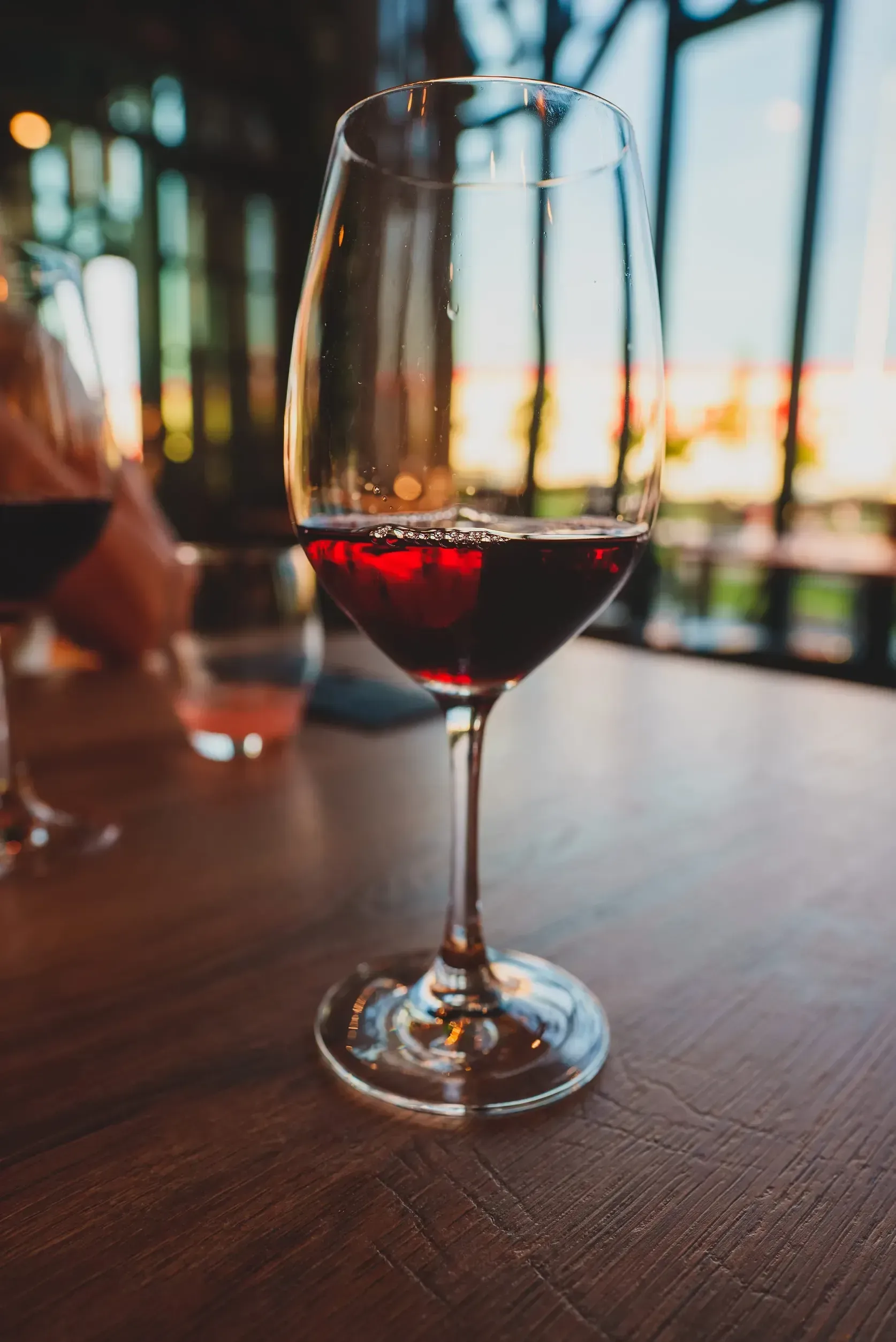 Una copa de vino tinto sobre una mesa de madera en un restaurante con iluminación tenue.