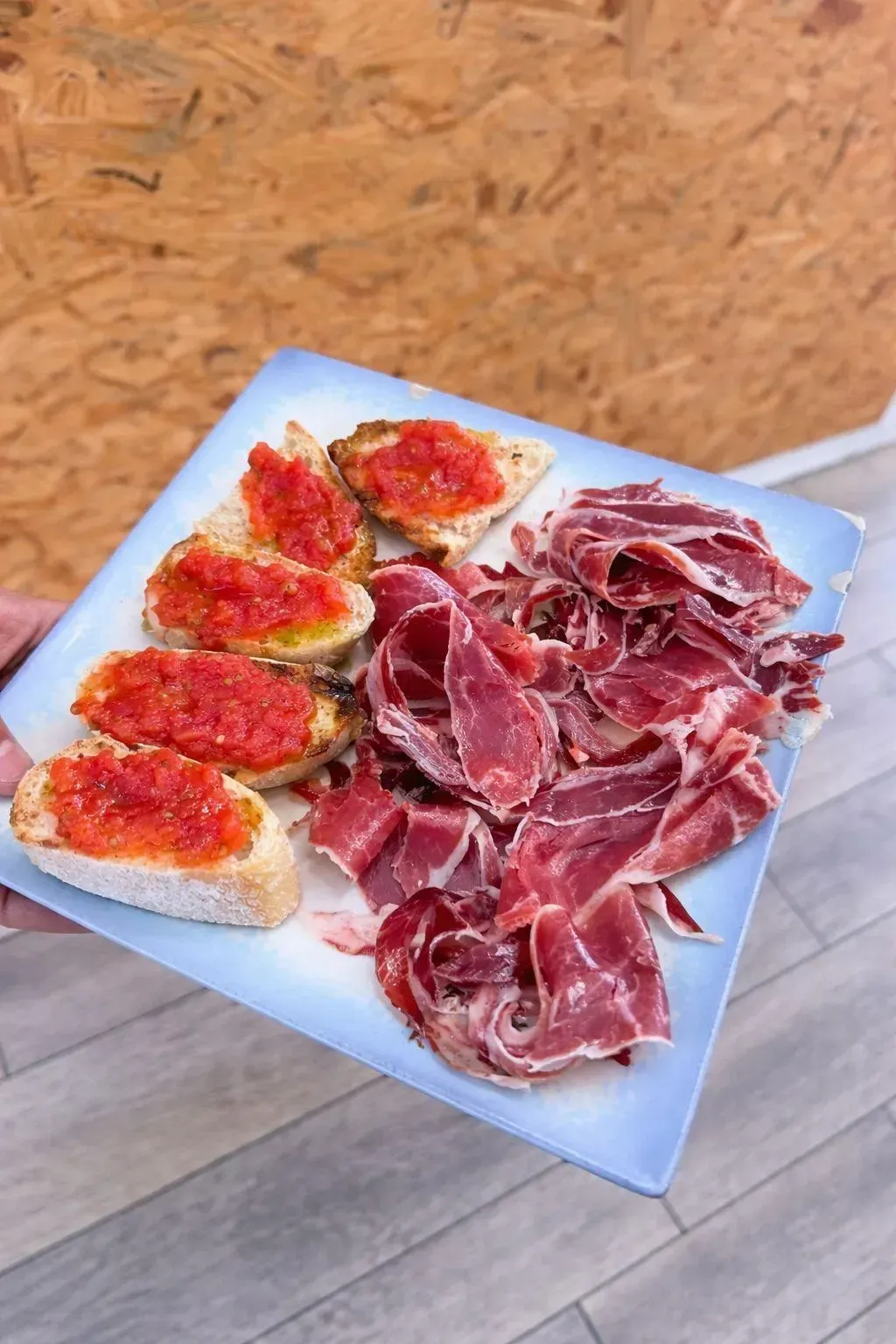 Plato con tostada untada con crema roja y una montaña de jamón curado en lonchas finas.