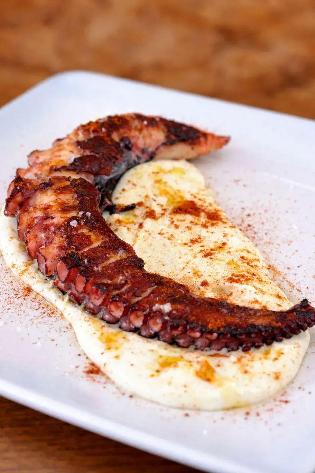 Pulpo a la plancha sobre puré de patatas cremoso en un plato blanco, espolvoreado con pimentón.