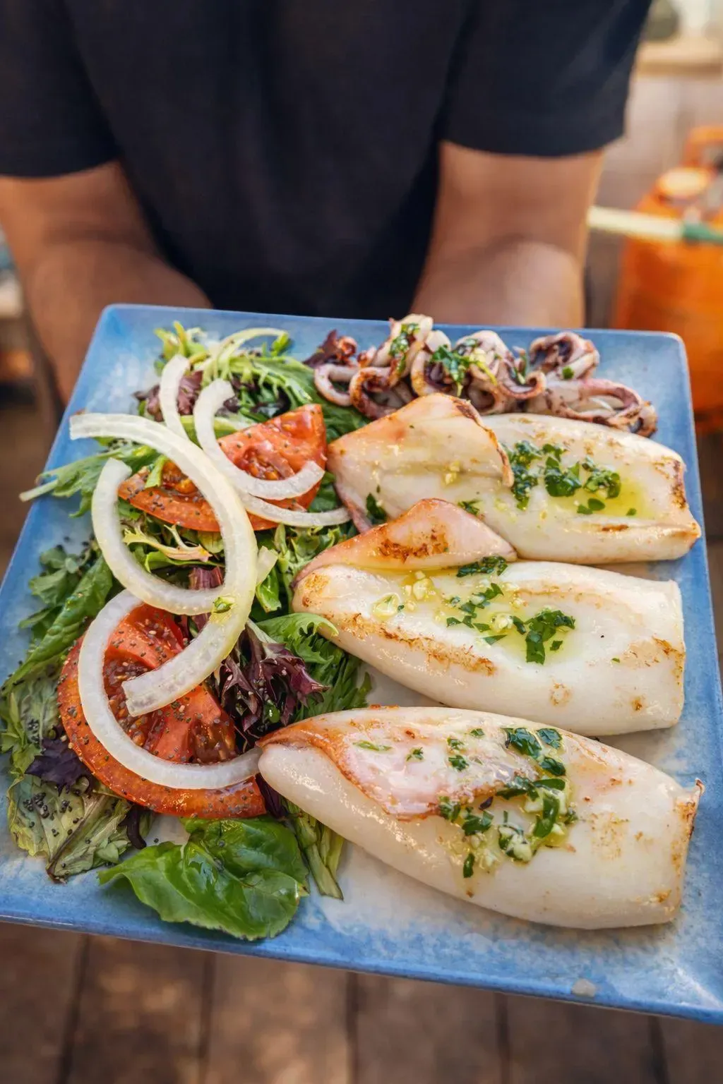 Ensalada de calamares emplatada con aros de cebolla y hierbas en un plato cuadrado azul.