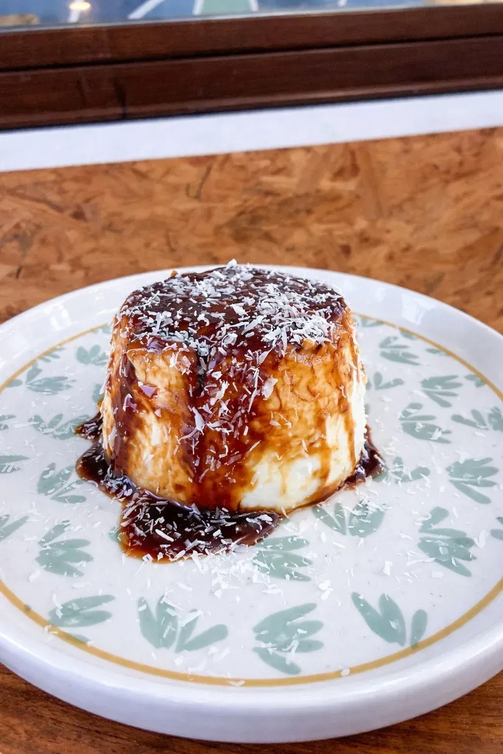 Flan de caramelo cubierto con coco rallado sobre un plato blanco decorado con flores.