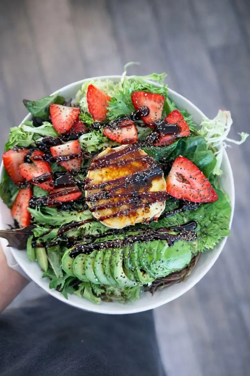 Un bol de ensalada con aguacate, fresas, verduras y pollo a la parrilla, rociado con glaseado balsámico.