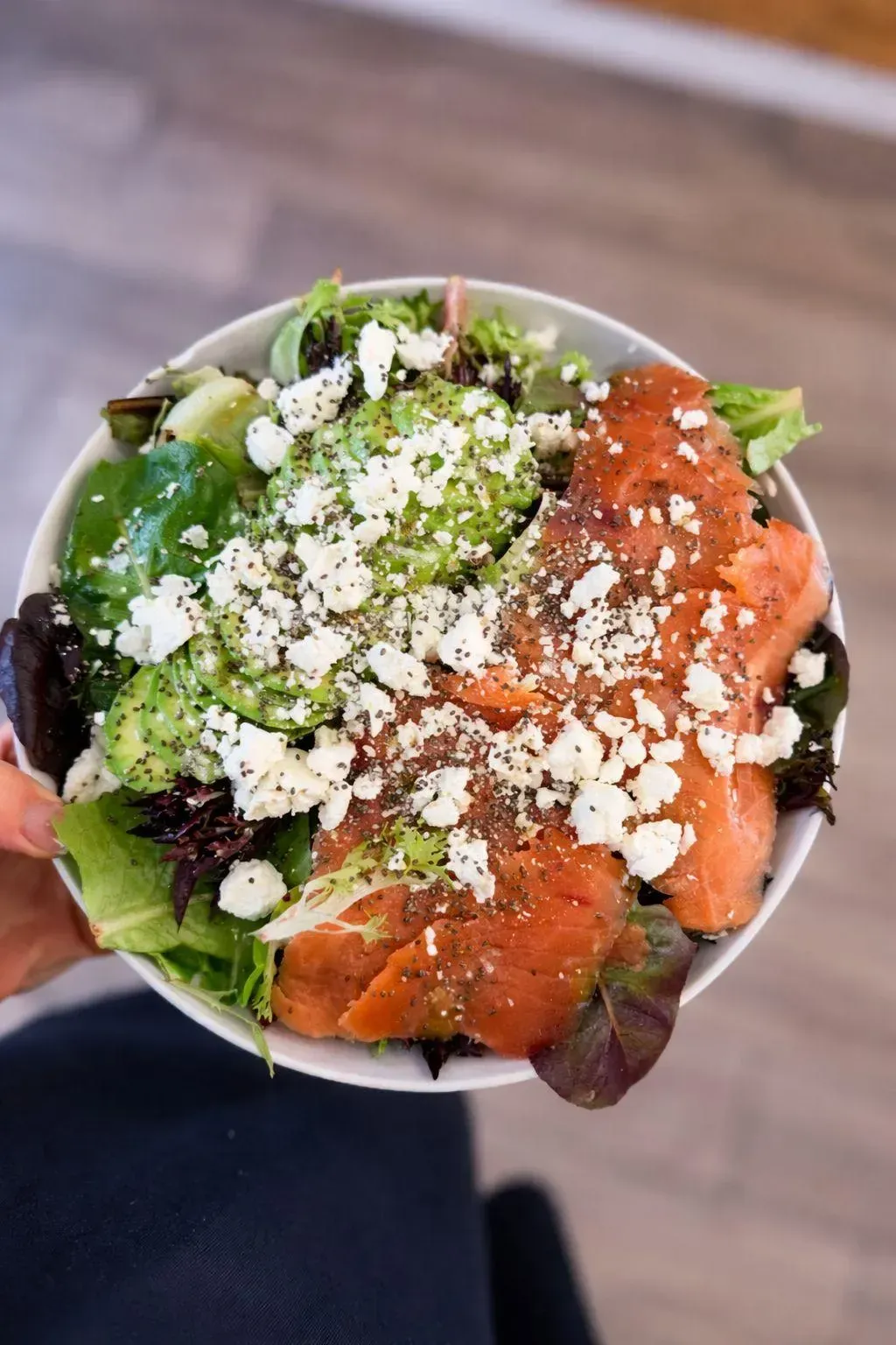 Ensalada colorida en un bol con hojas verdes, aguacate, salmón y queso desmenuzado.
