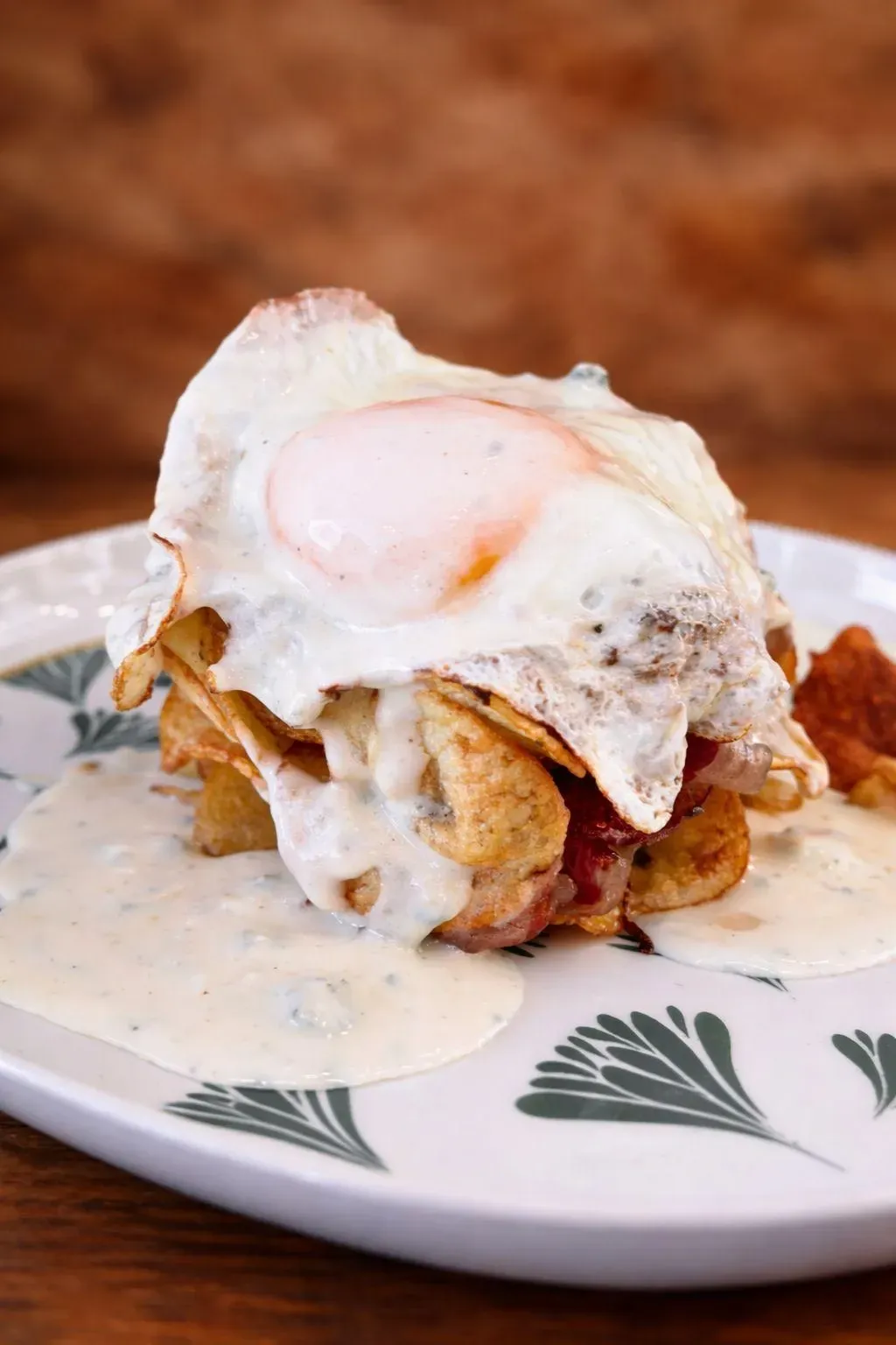 Huevo frito sobre una pila de comida con salsa cremosa en un plato estampado.