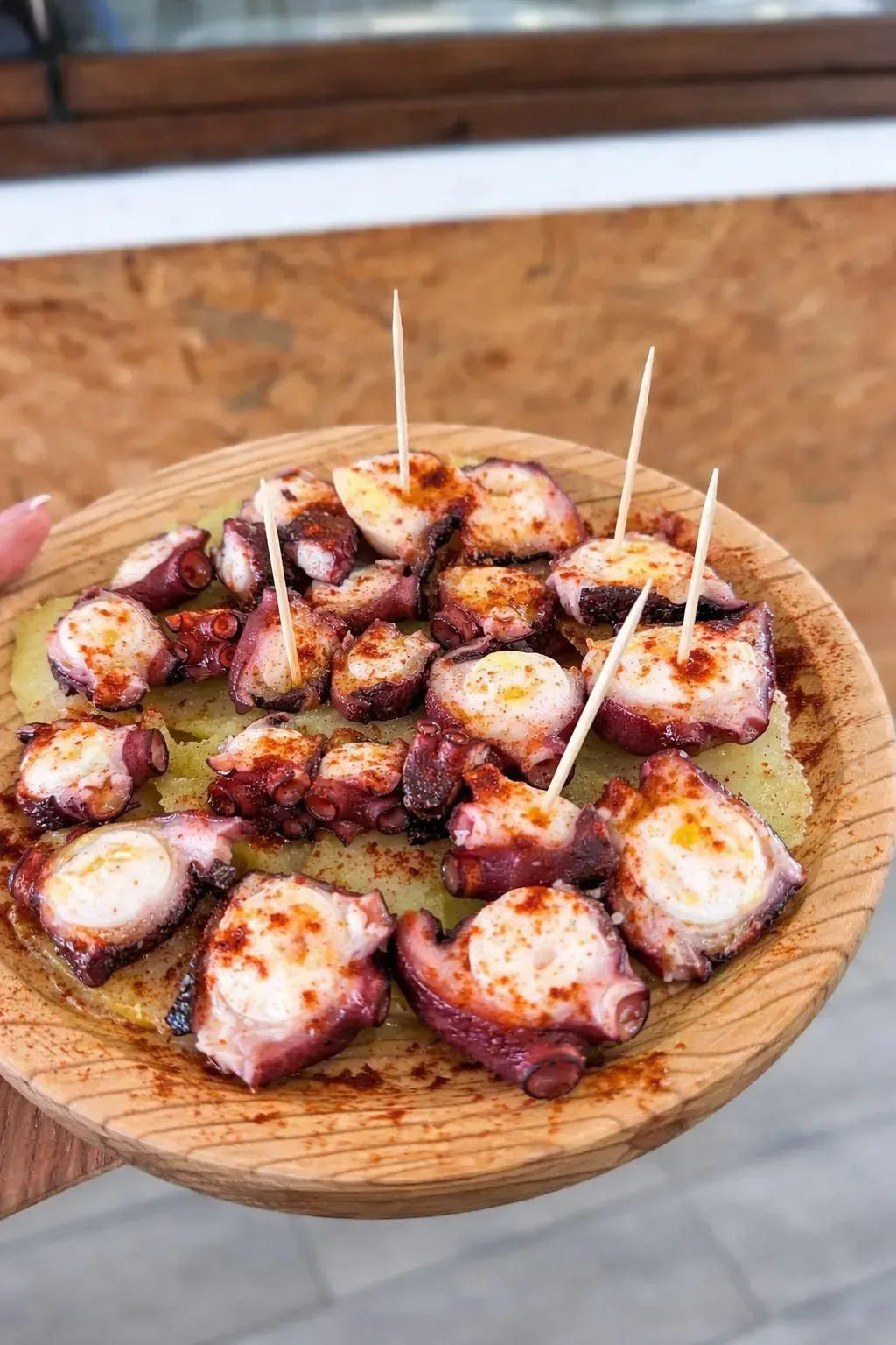 Trozos de pulpo a la parrilla sobre un plato de madera, aderezados con especias y palillos de dientes.