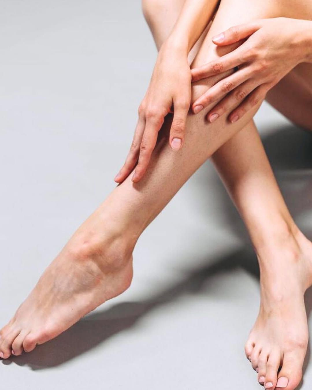 Piernas y manos desnudas sobre una superficie gris. Una mano descansa sobre la pierna.