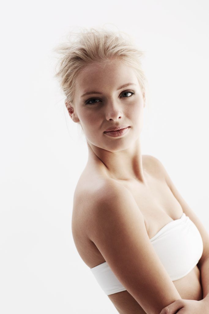 Mujer con diadema y bata blancas, acostada con los ojos cerrados, probablemente sometiéndose a un tratamiento facial.