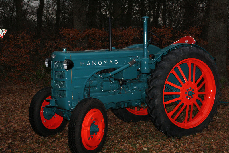 Ein blauer Hanomag Traktor mit roten Rädern steht im Wald