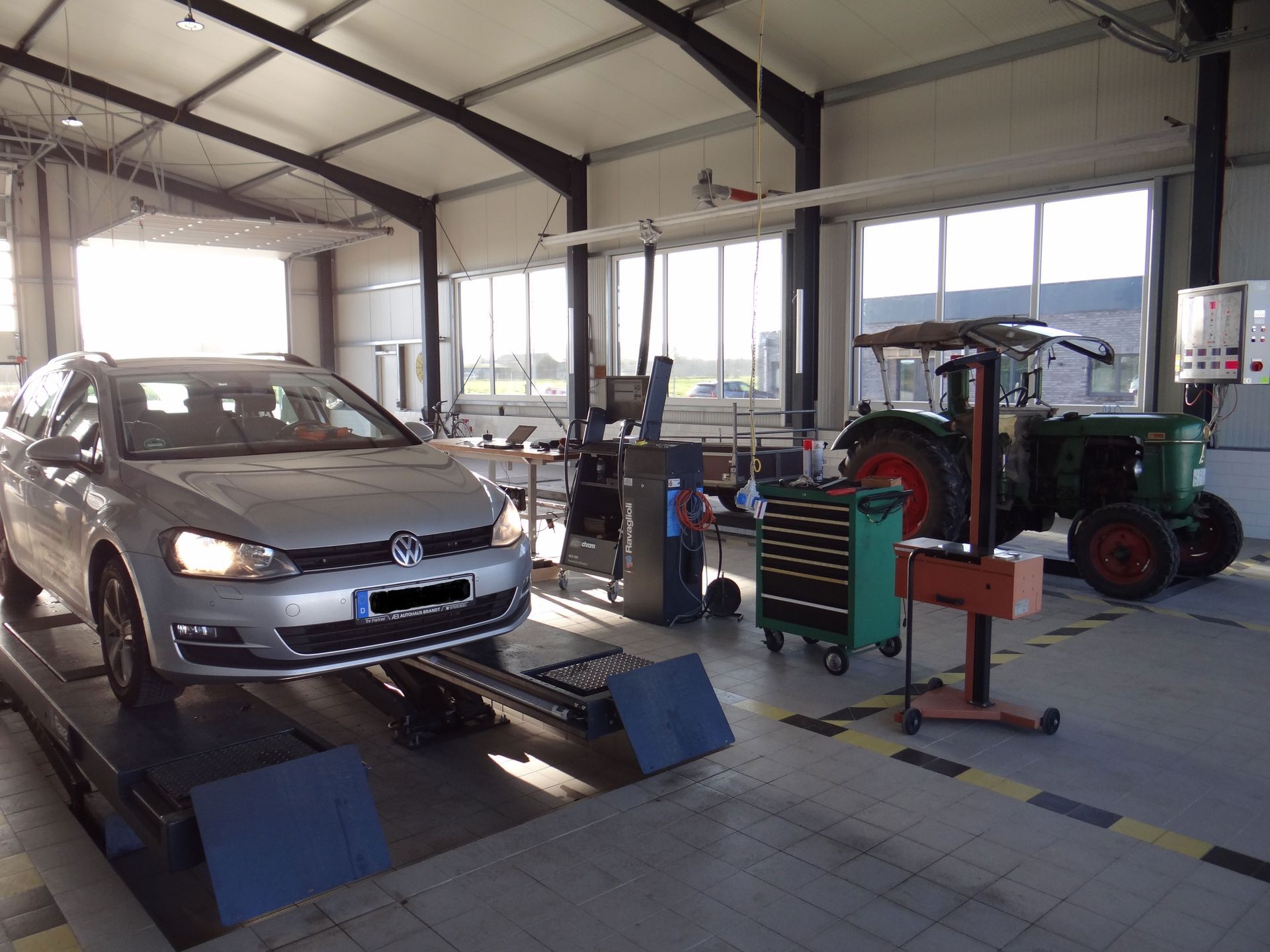 In einer Garage steht ein Auto auf einer Hebebühne neben einem Traktor.