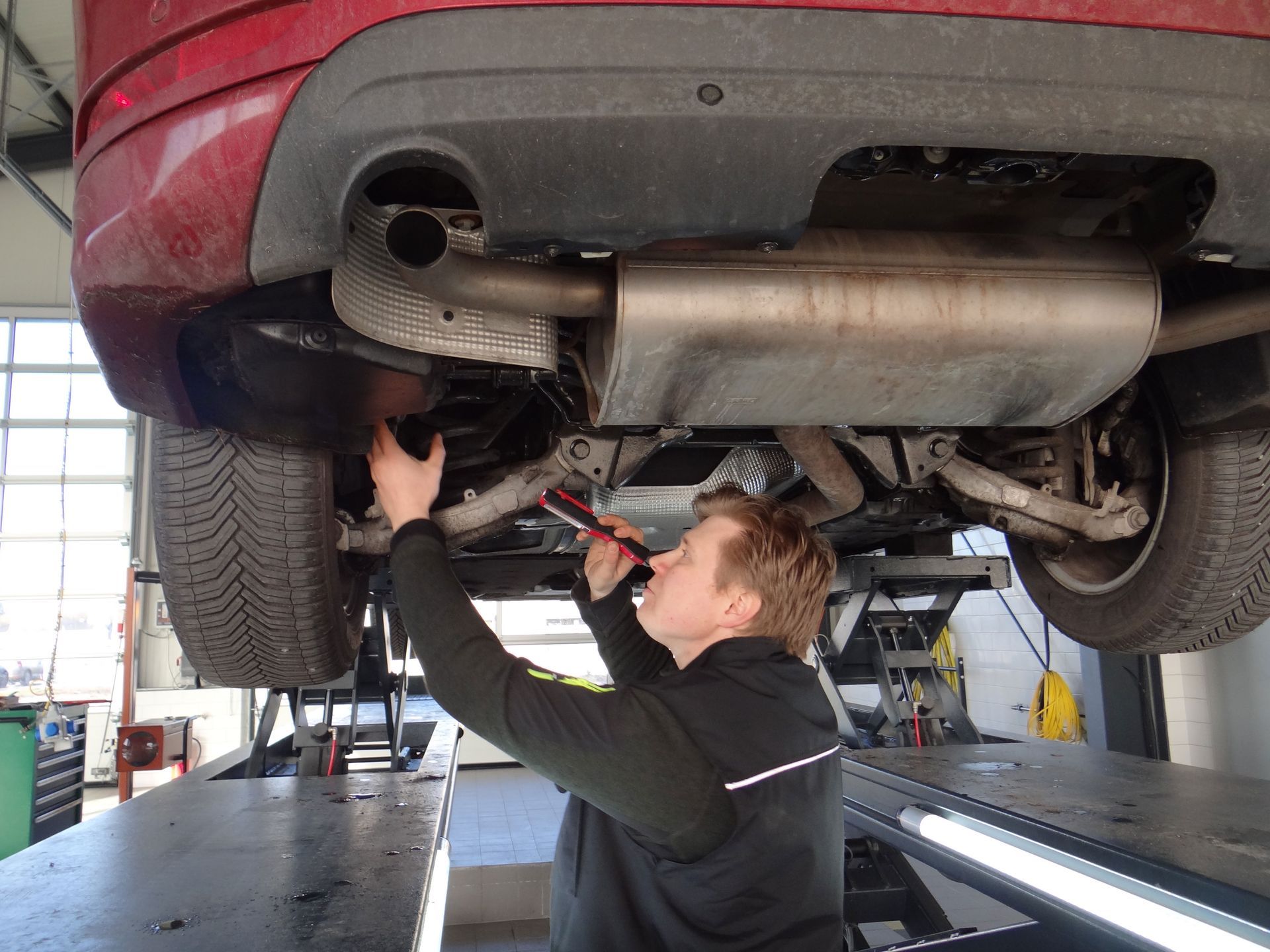 Ein Mann arbeitet in einer Garage unter einem roten Auto.