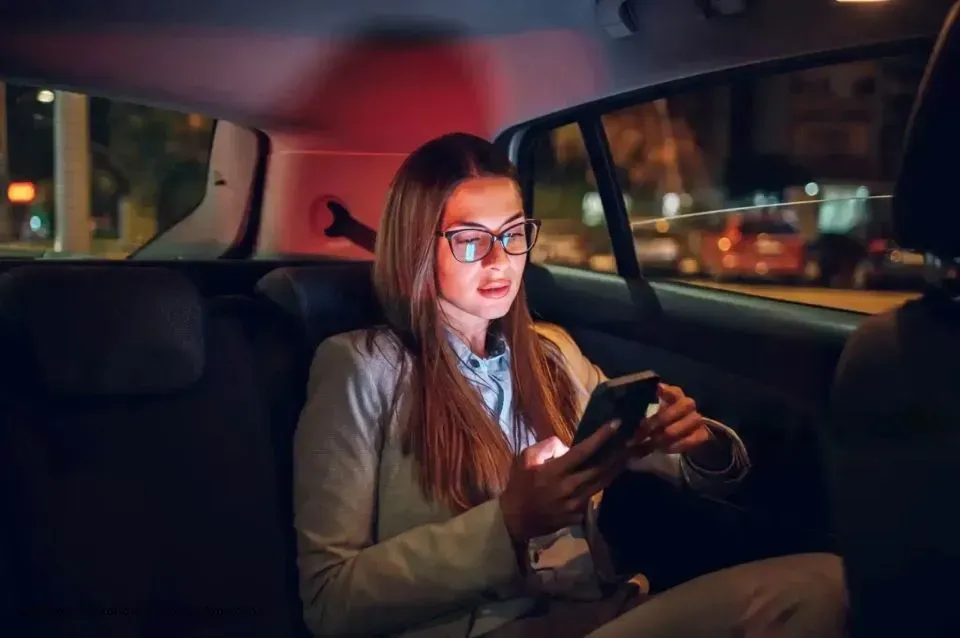Person mit langen Haaren sitzt nachts im Auto, schaut Smartphone