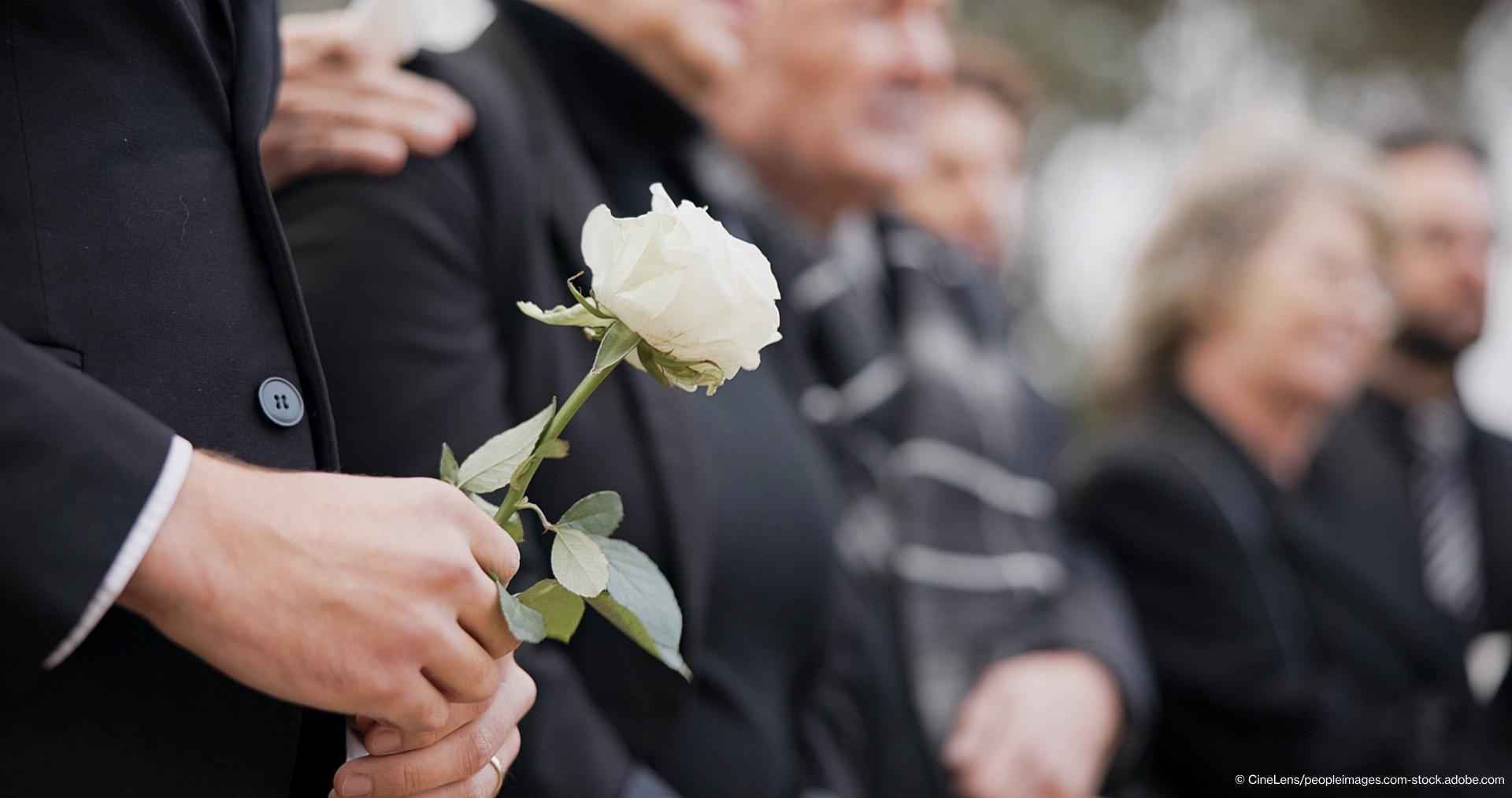 Person bei einer Beerdigung auf einem Friedhof, die in Trauer ist und bei einer Gedenkfeier um einen Verlust trauert.