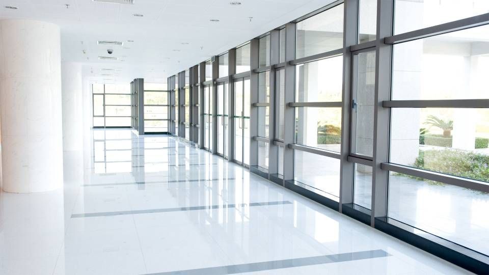 Couloir de bureau lumineux et vide, avec de grandes fenêtres allant du sol au plafond et un sol blanc brillant