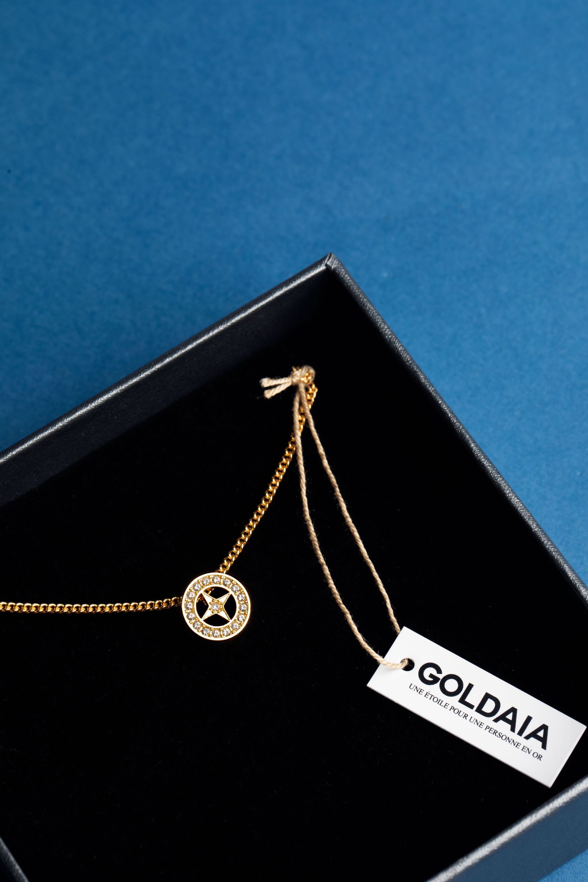 Collier en or avec étiquette dans une boîte noire sur fond bleu