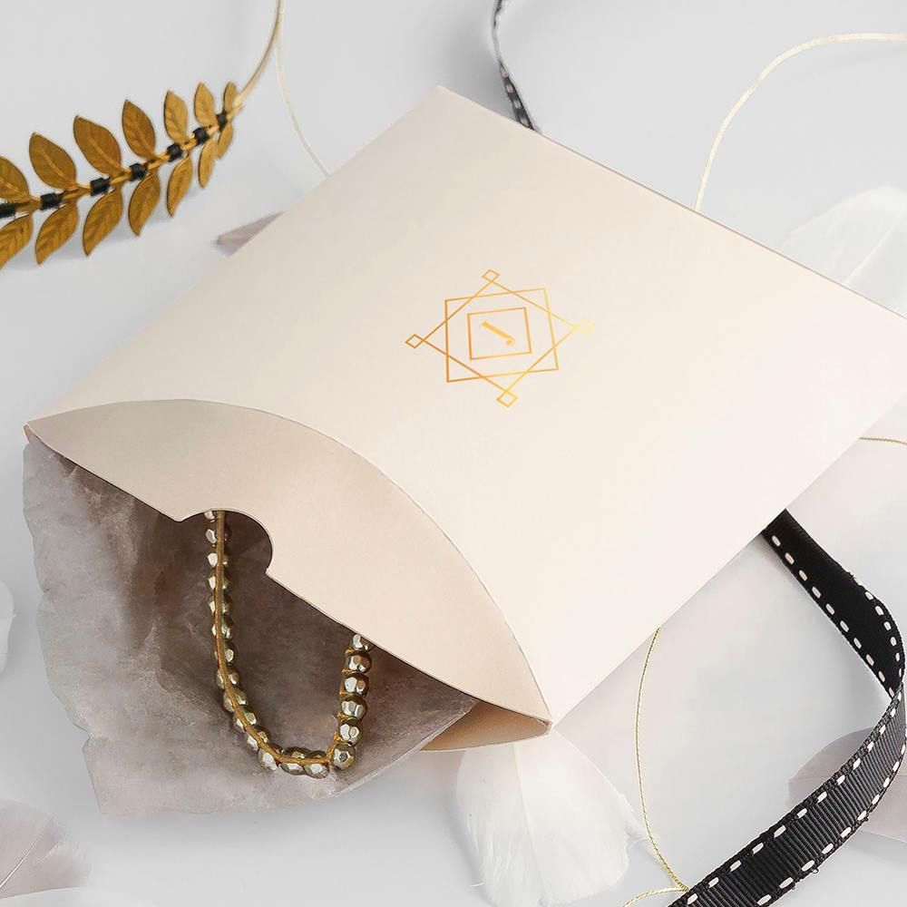 Berlingot avec un logo géométrique doré, contenant un collier de perles dorées