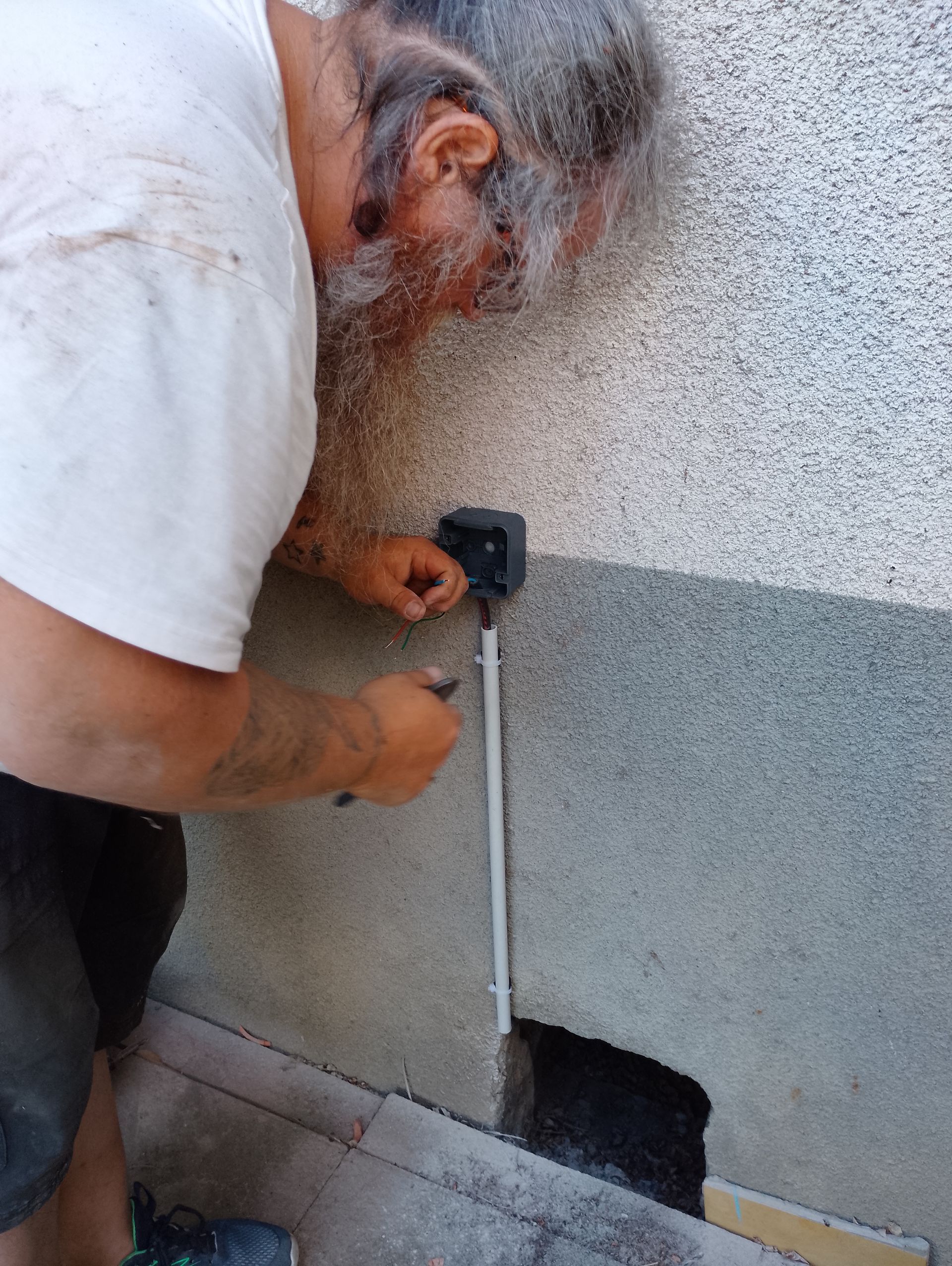 Electricien utilisant un outil pour installer une  prise en extérieur