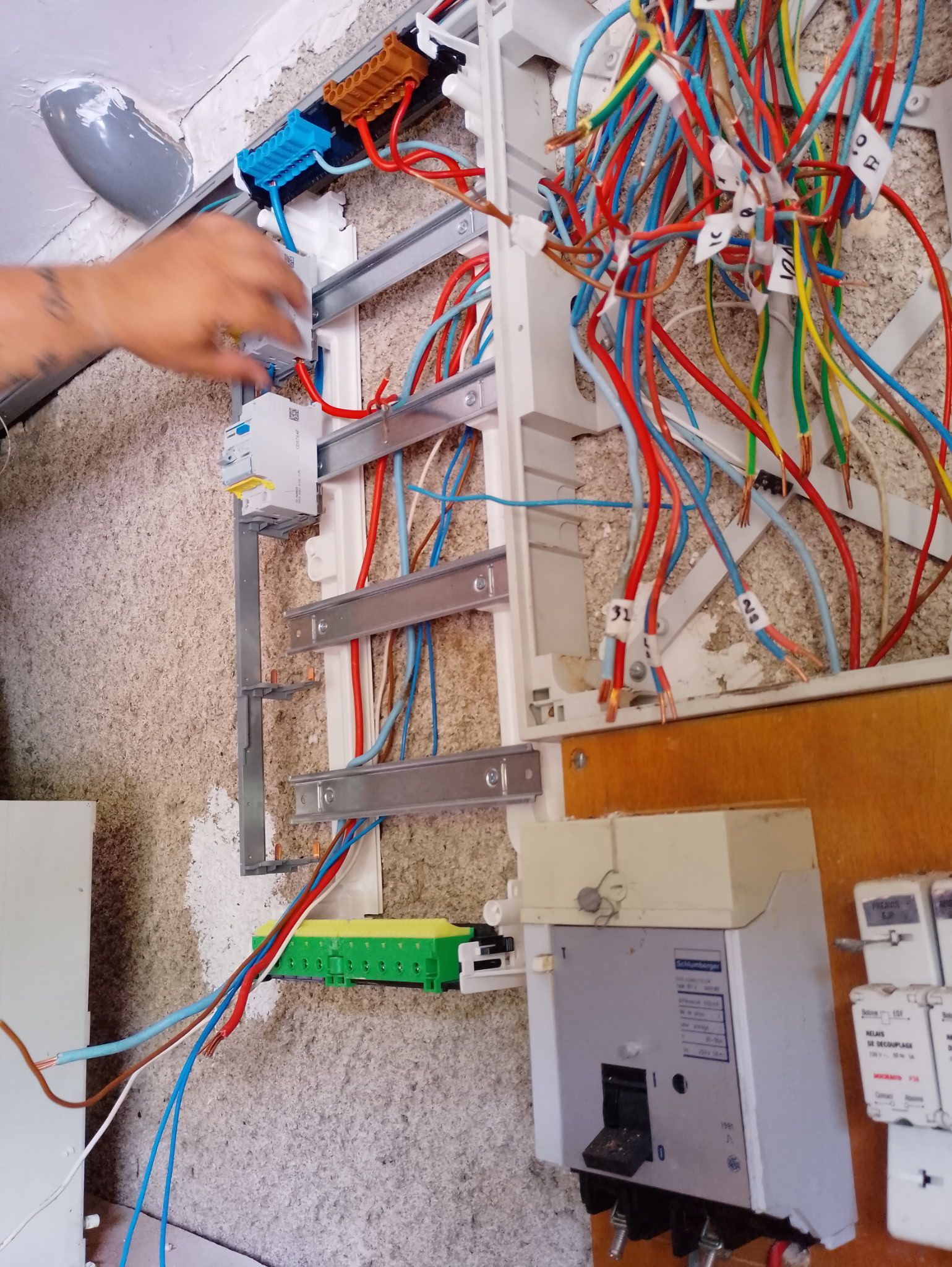 Tableau électrique avec câblage multicolore apparent et une main qui travaille à l'intérieur.