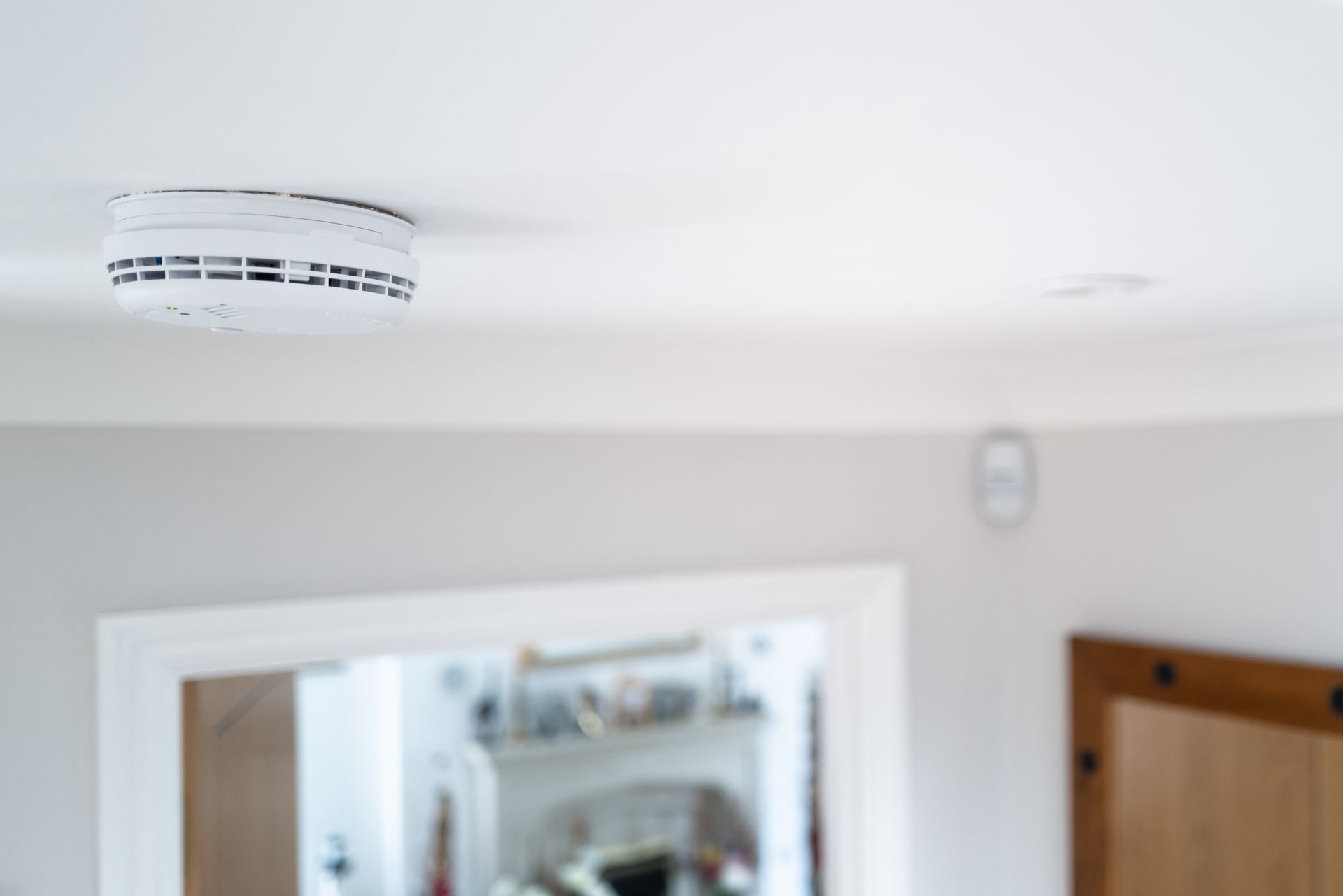Détecteur de fumée blanc au plafond, au-dessus d'une porte dans une pièce lumineuse.