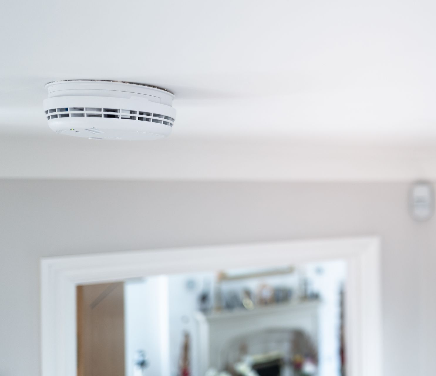 Détecteur de fumée blanc fixé au plafond au-dessus d'une porte dans une pièce lumineuse.