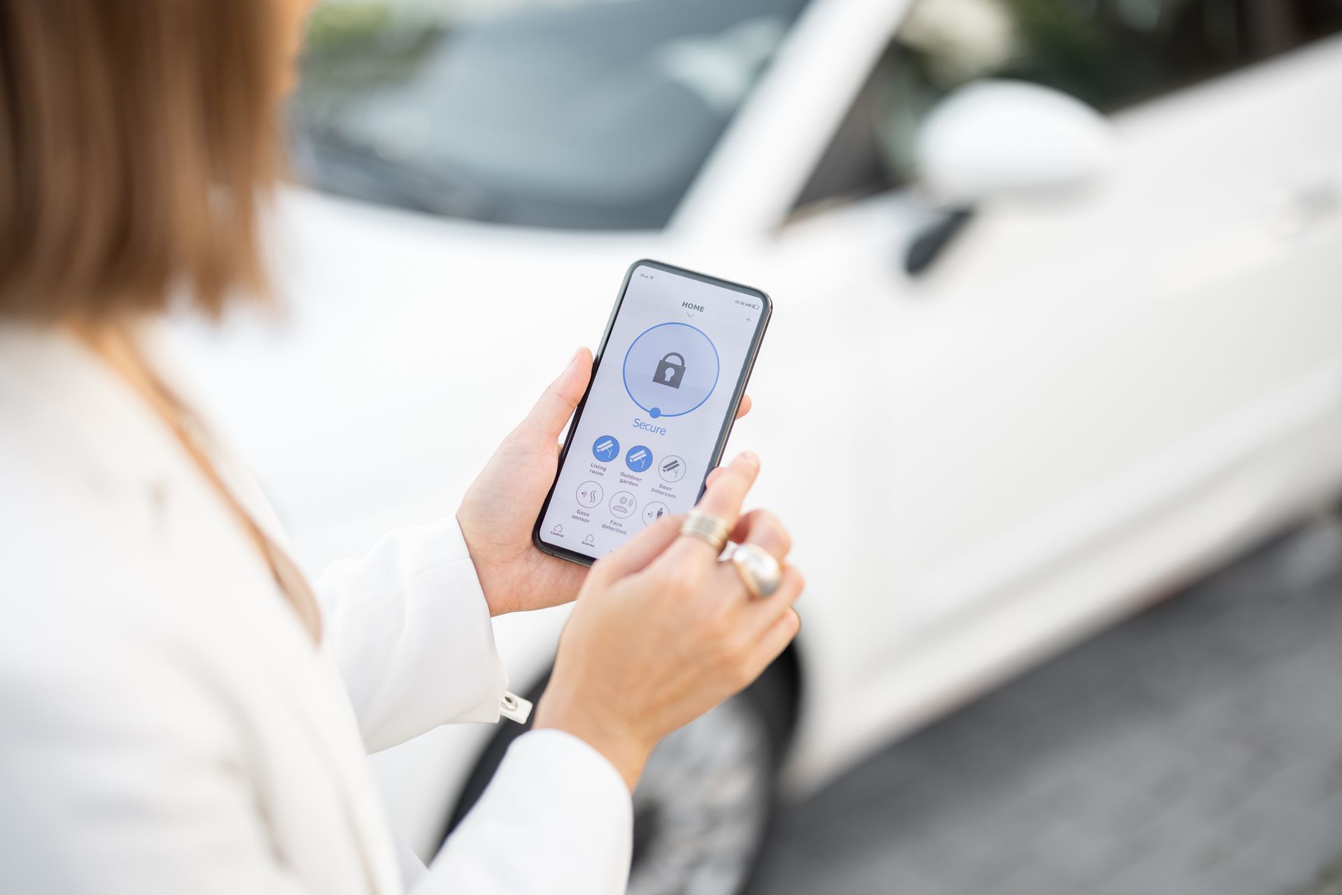 Une personne tenant un smartphone avec une application pour voiture devant une voiture blanche.