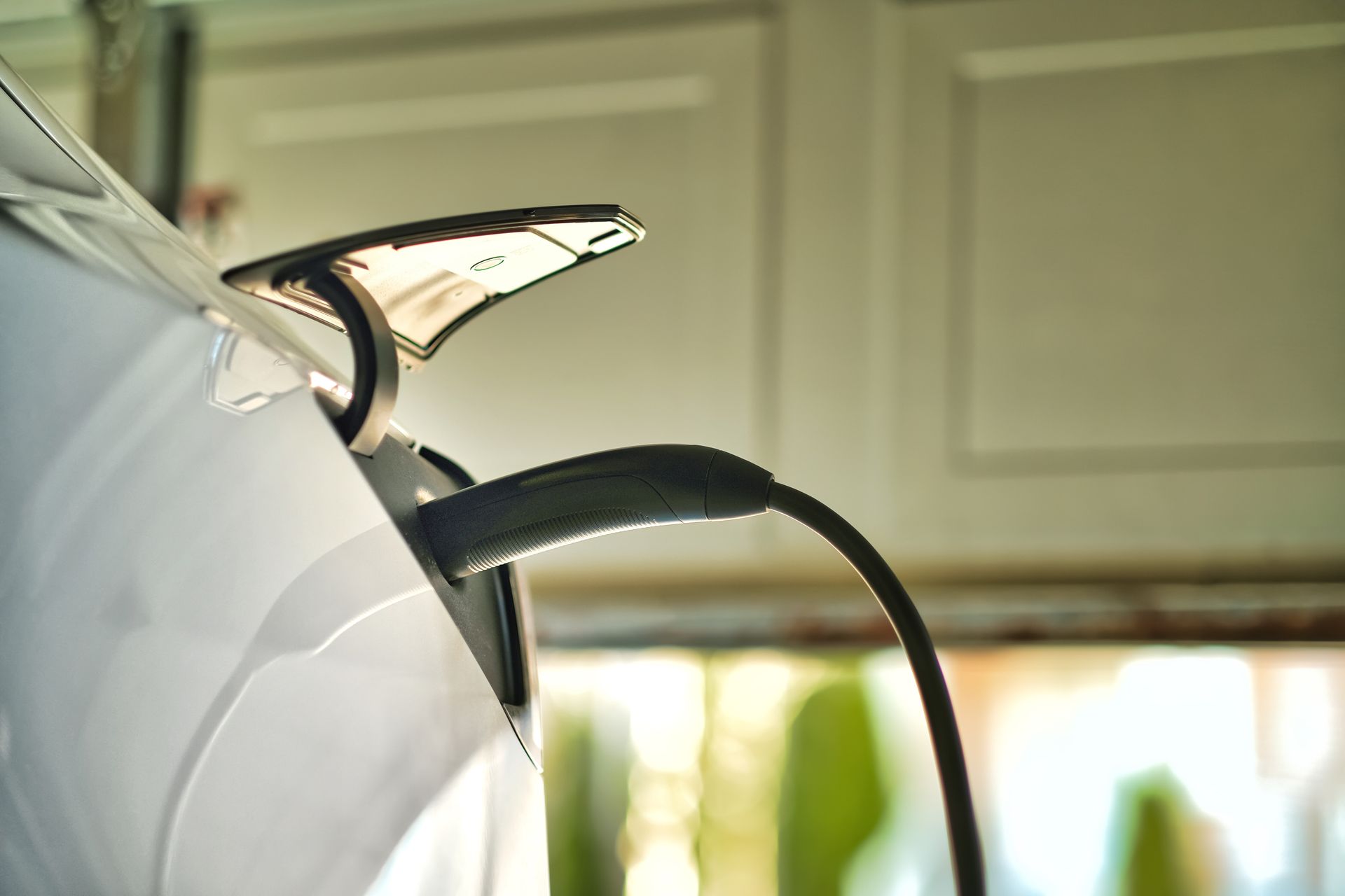 Gros plan sur une voiture blanche en charge à une borne de recharge pour véhicules électriques, avec un câble noir branché.