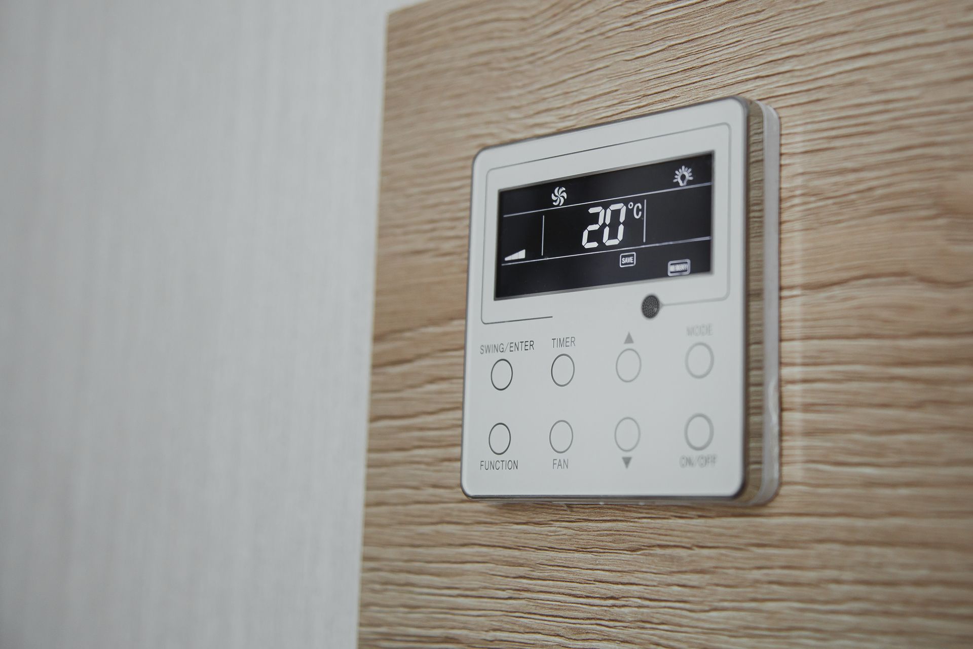 Thermostat numérique mural avec écran et boutons tactiles, intégré à un mur lambrissé.