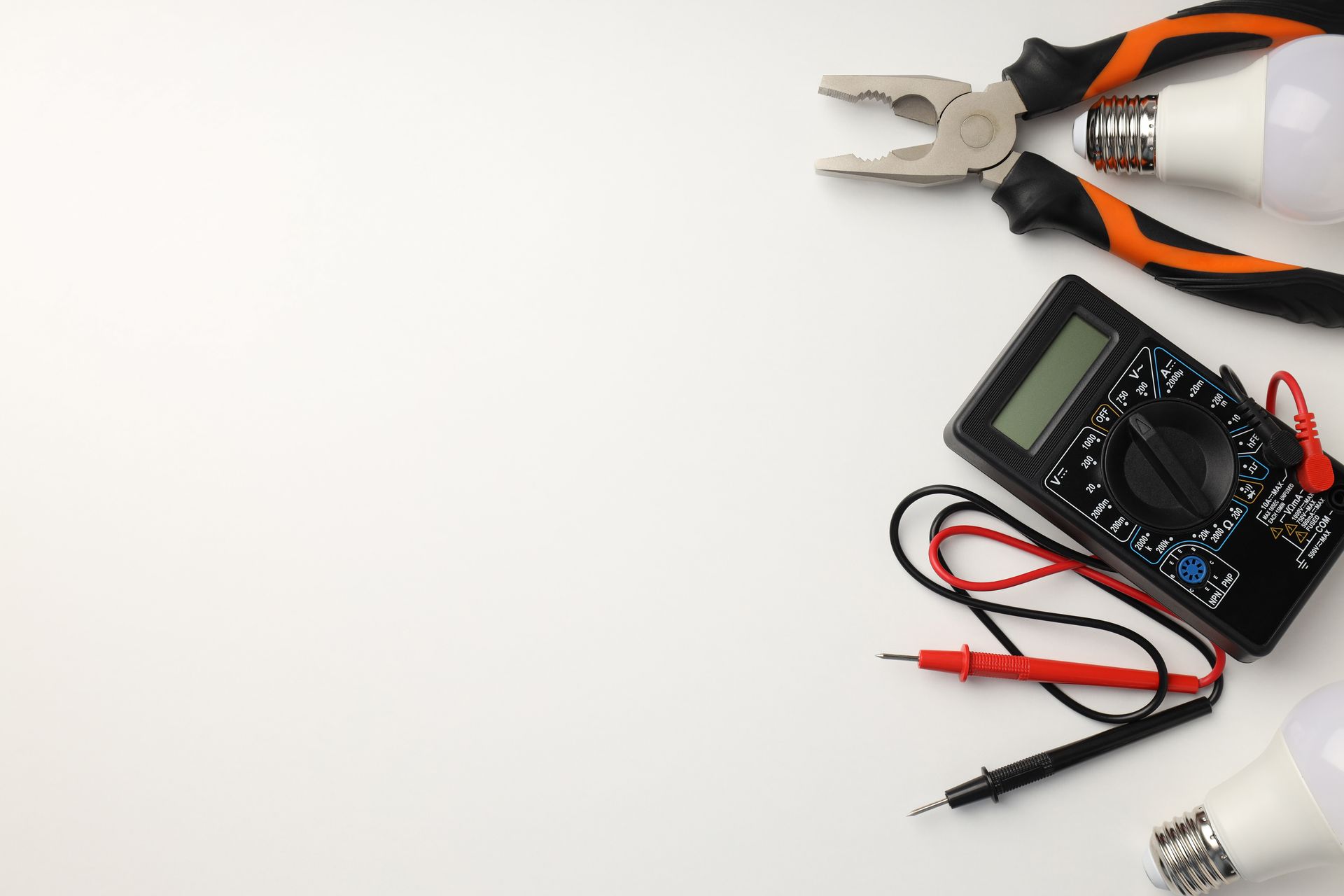 Multimètre avec sondes rouge et noire à côté d'une pince à poignée orange sur une surface blanche.