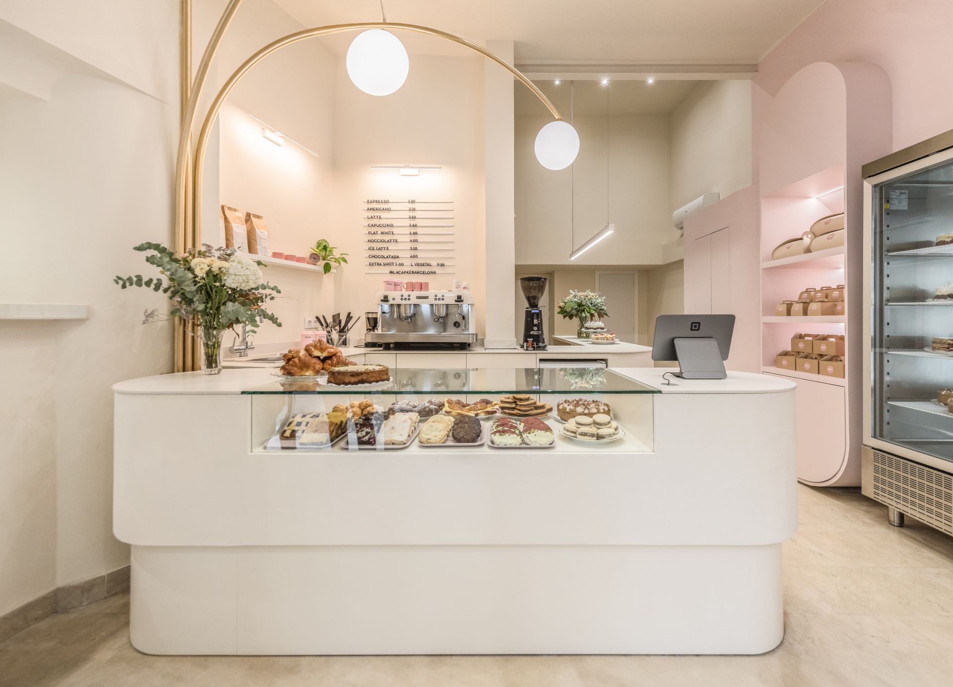 Panadería minimalista de color rosa con mostrador blanco y pasteles bajo cálidas luces colgantes.