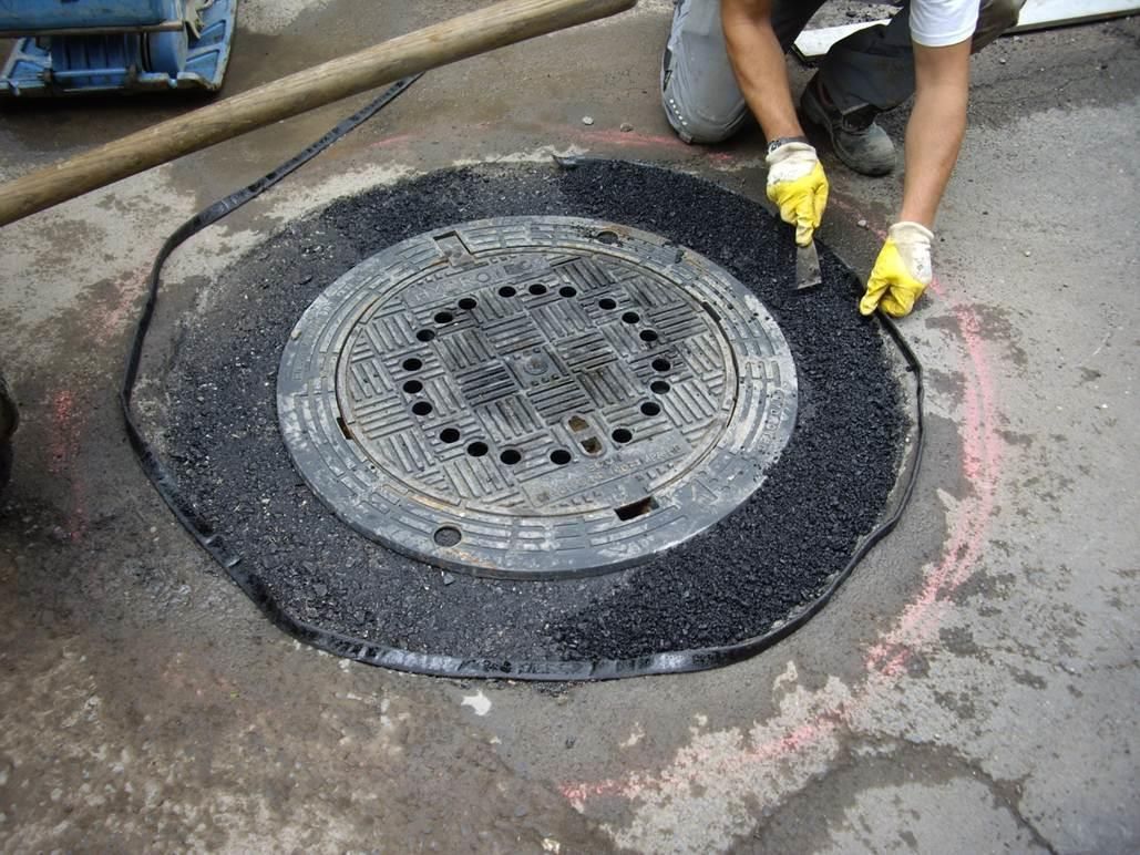 Ein Schachtdeckel wird von einer Person mit gelben Handschuhen repariert