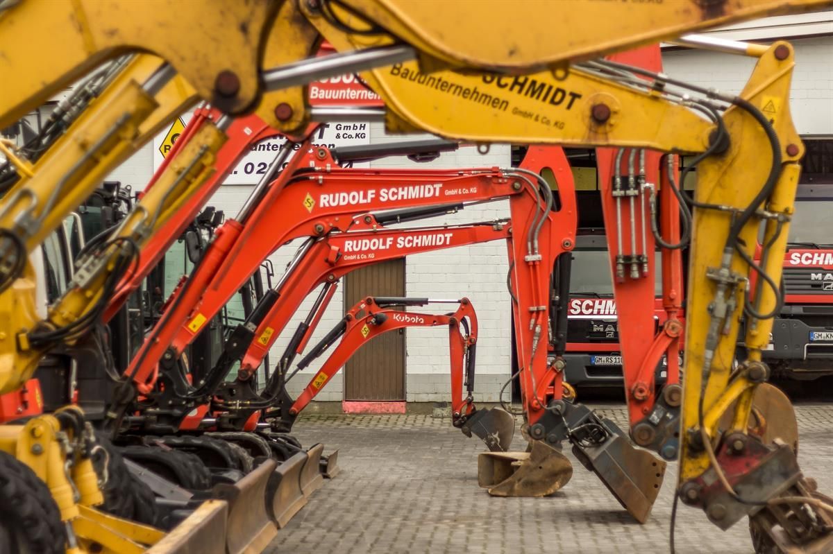 Eine Reihe von Baggern parkt vor einem Gebäude mit der Aufschrift „Rudolf Schmidt“