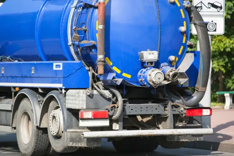 Camión tanque séptico azul estacionado en una calle con una manguera conectada.