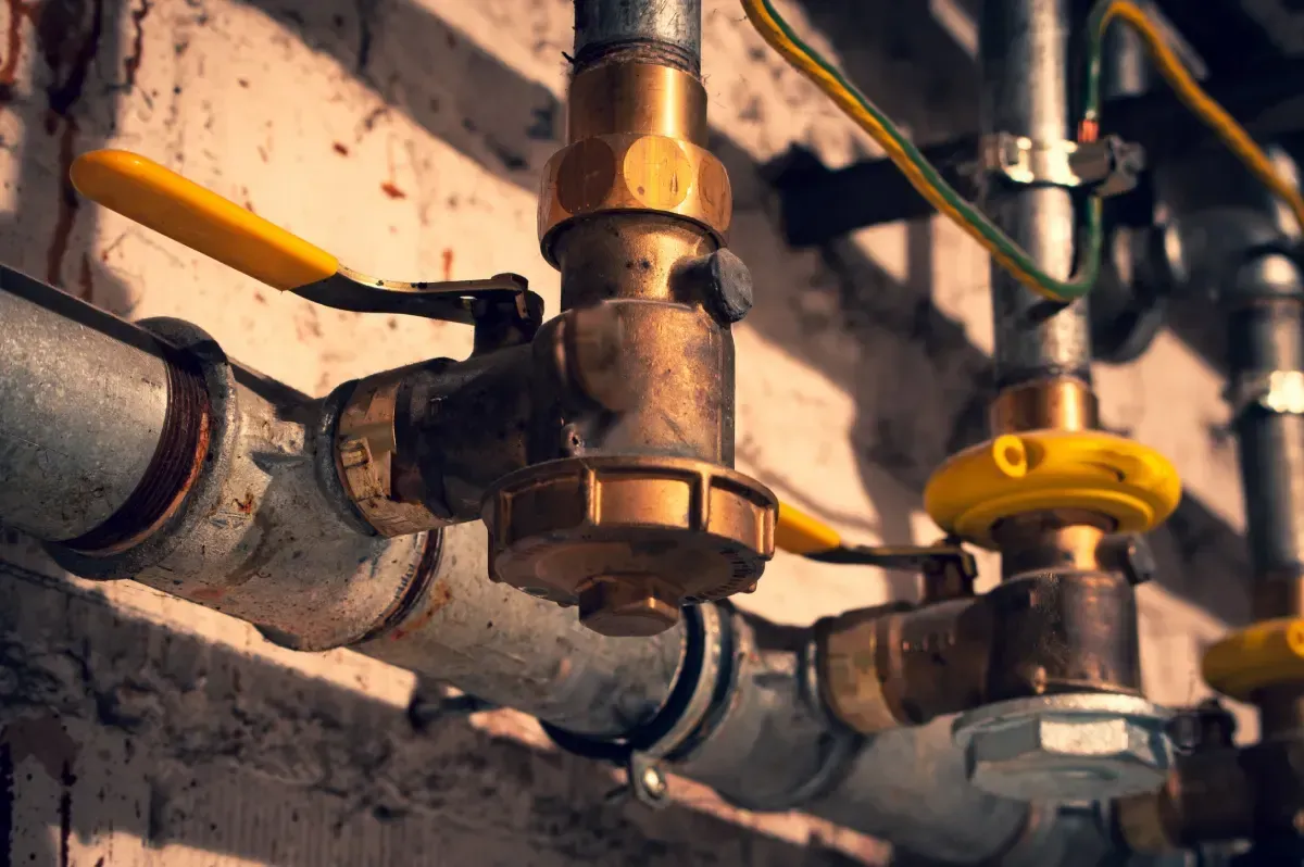 Tubos con válvulas de latón y manijas amarillas, contra una pared rugosa.