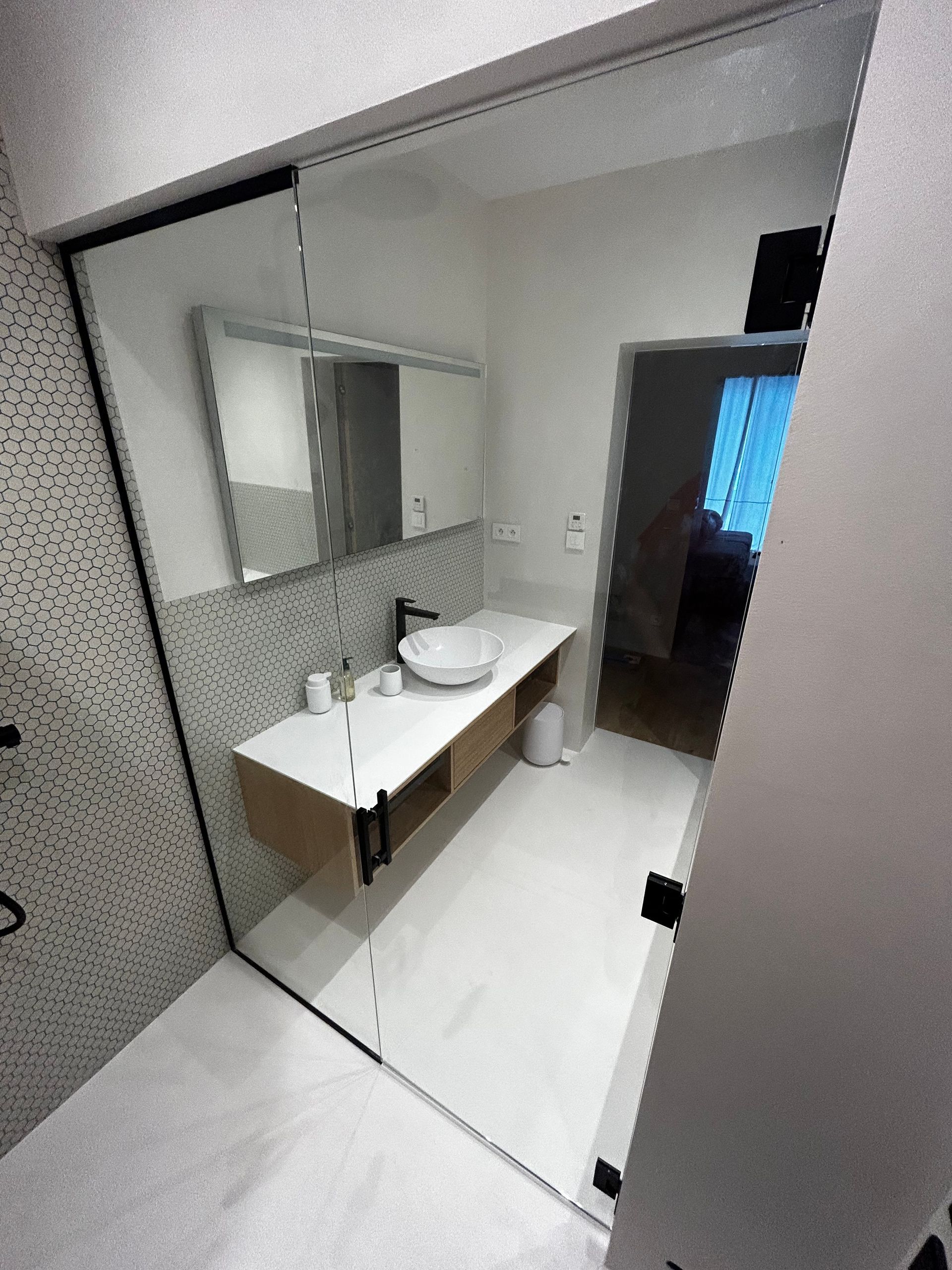 Petite salle de bains avec lavabo mural, grand miroir et murs et sol carrelés.