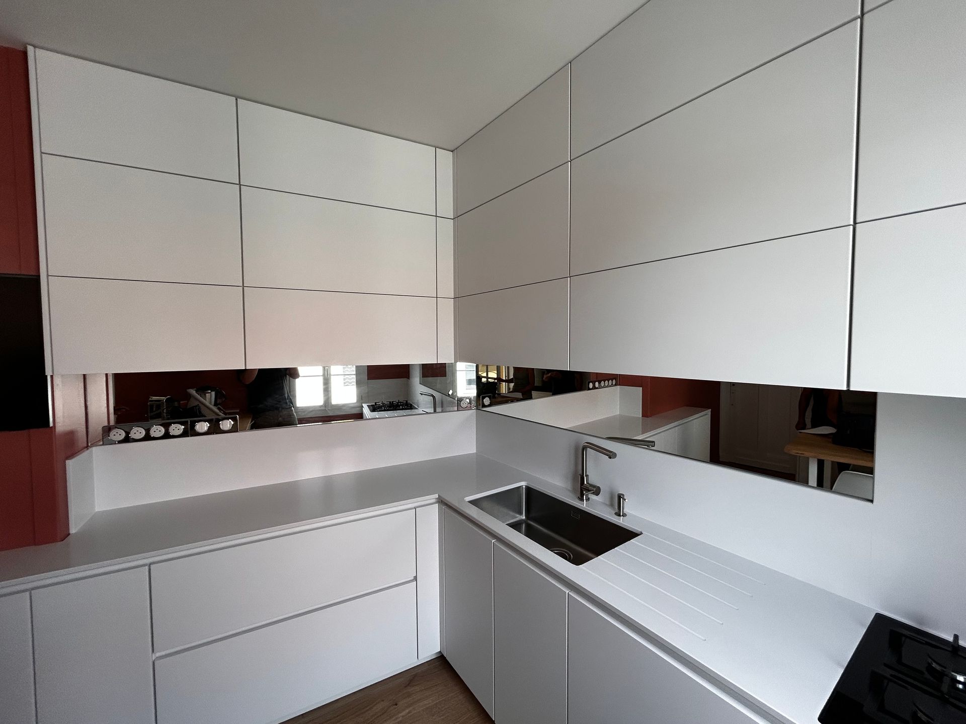 Cuisine blanche moderne avec des armoires épurées, une crédence en miroir, un évier noir et des comptoirs minimalistes.