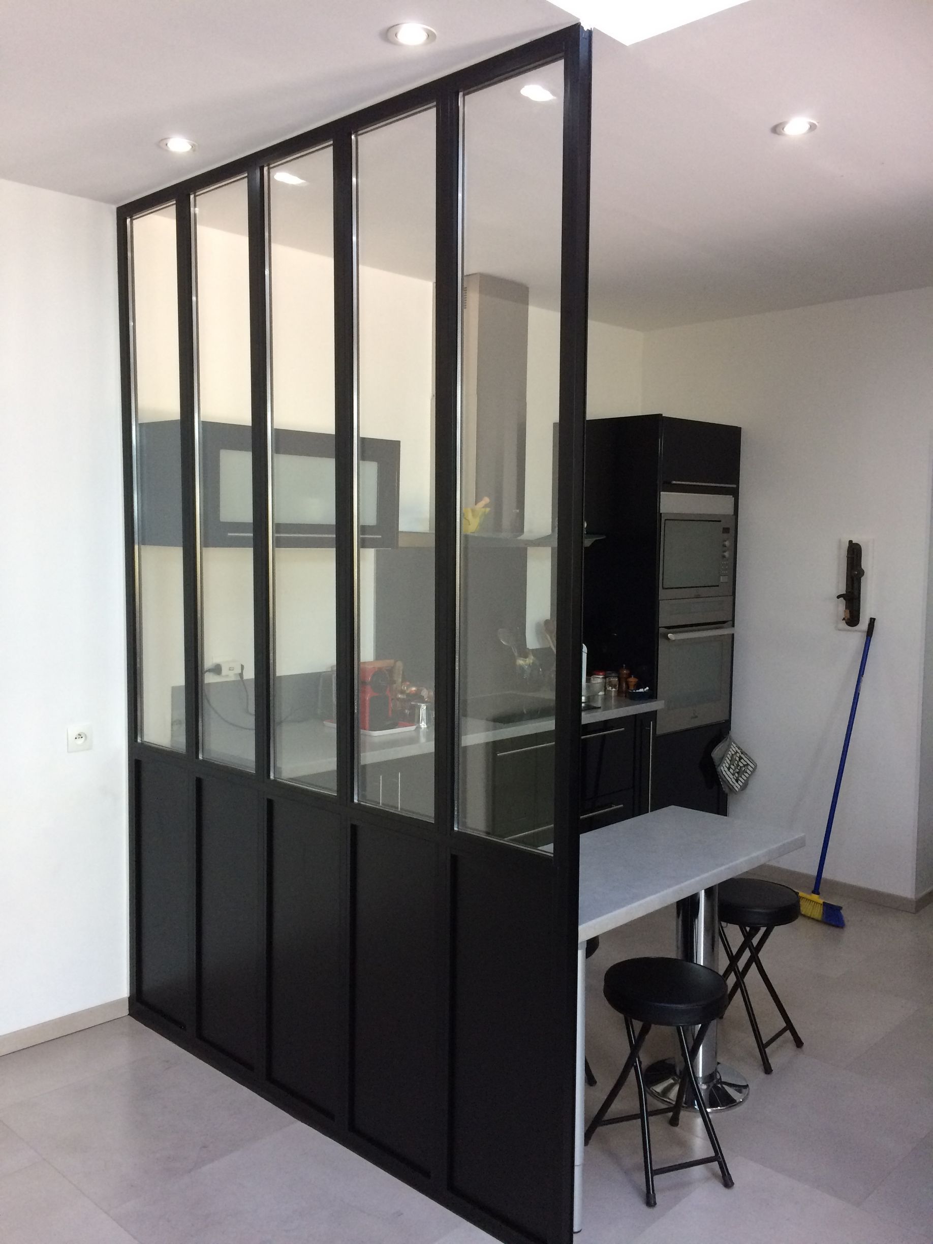 Bureau moderne avec cloison vitrée à cadre noir, bureau, tabouret et produits d'entretien dans une pièce lumineuse